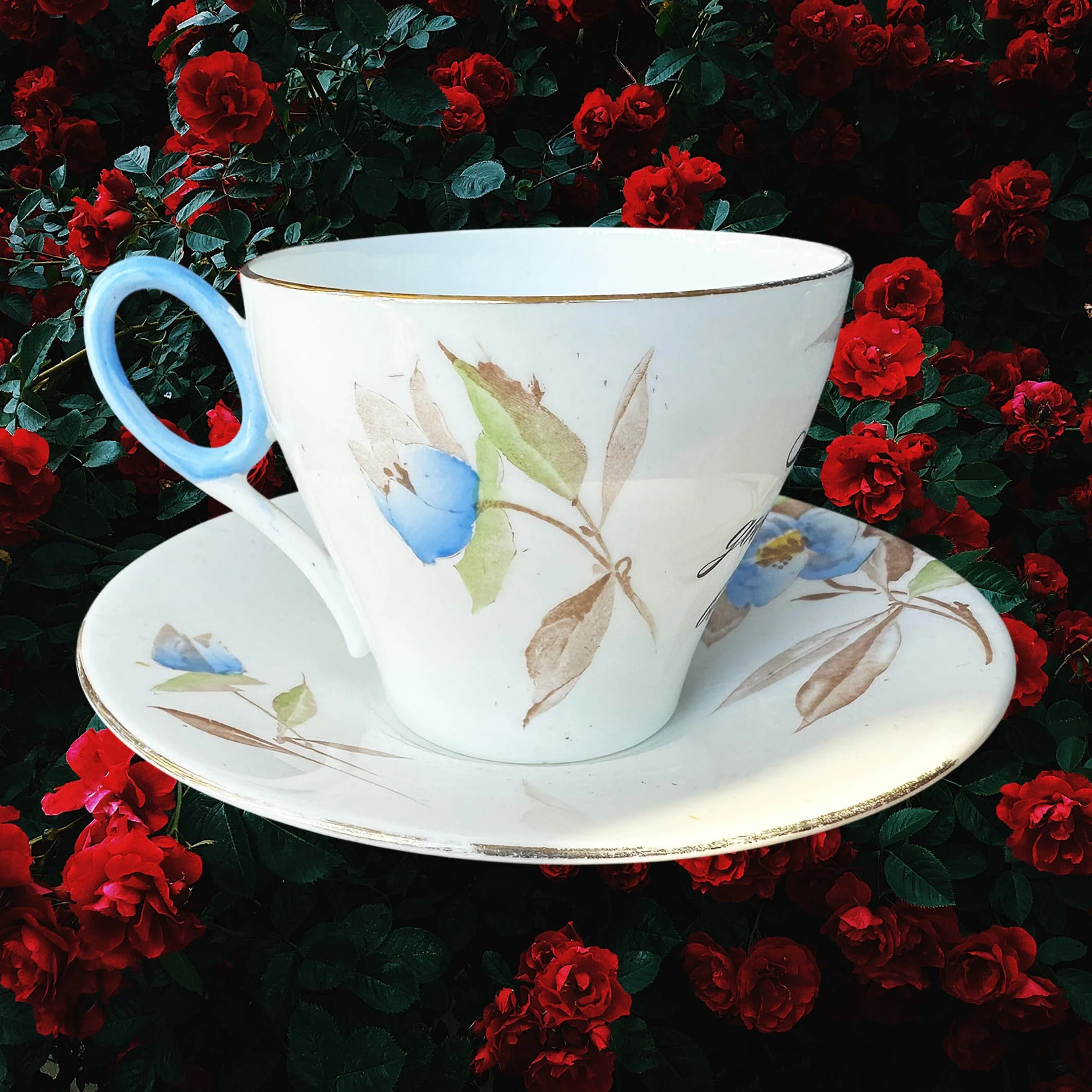 A vintage tea cup and saucer with a blue floral design and the words "let the good times be gin" in black cursive writing