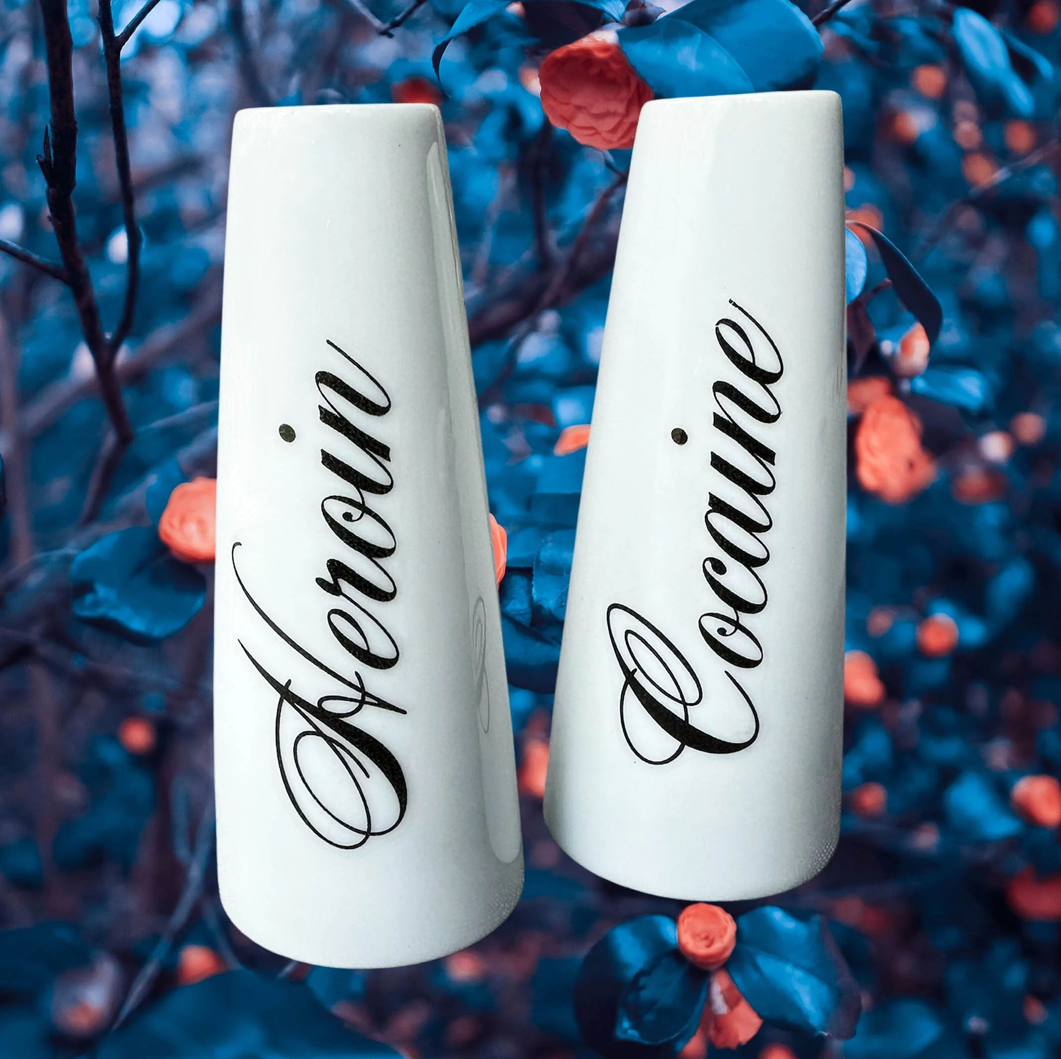 White salt and pepper shakers with the word “heroin” and “cocaine” in black cursive writing