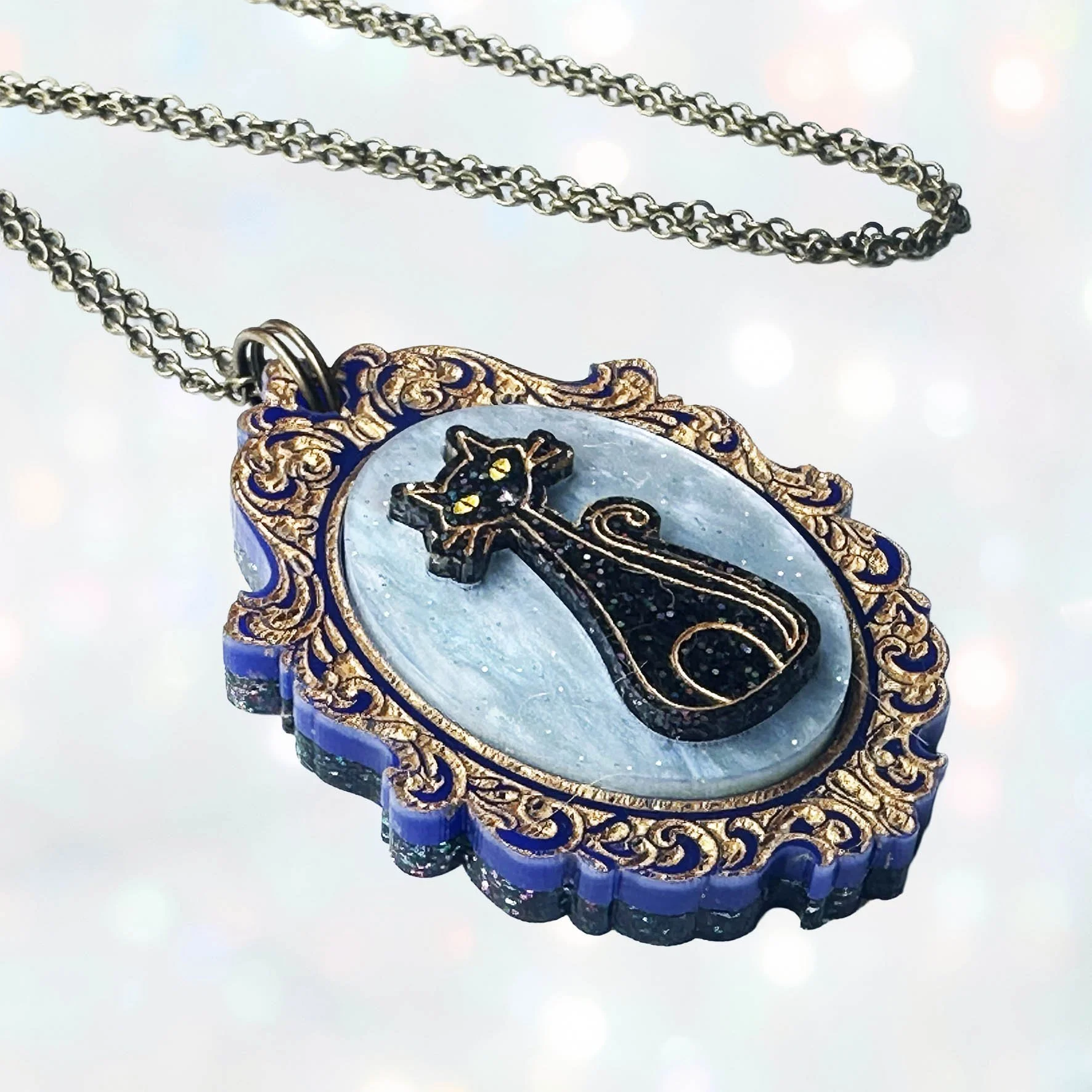 A laser cut acrylic cameo style necklace featuring a black cat inside inside a gold frame