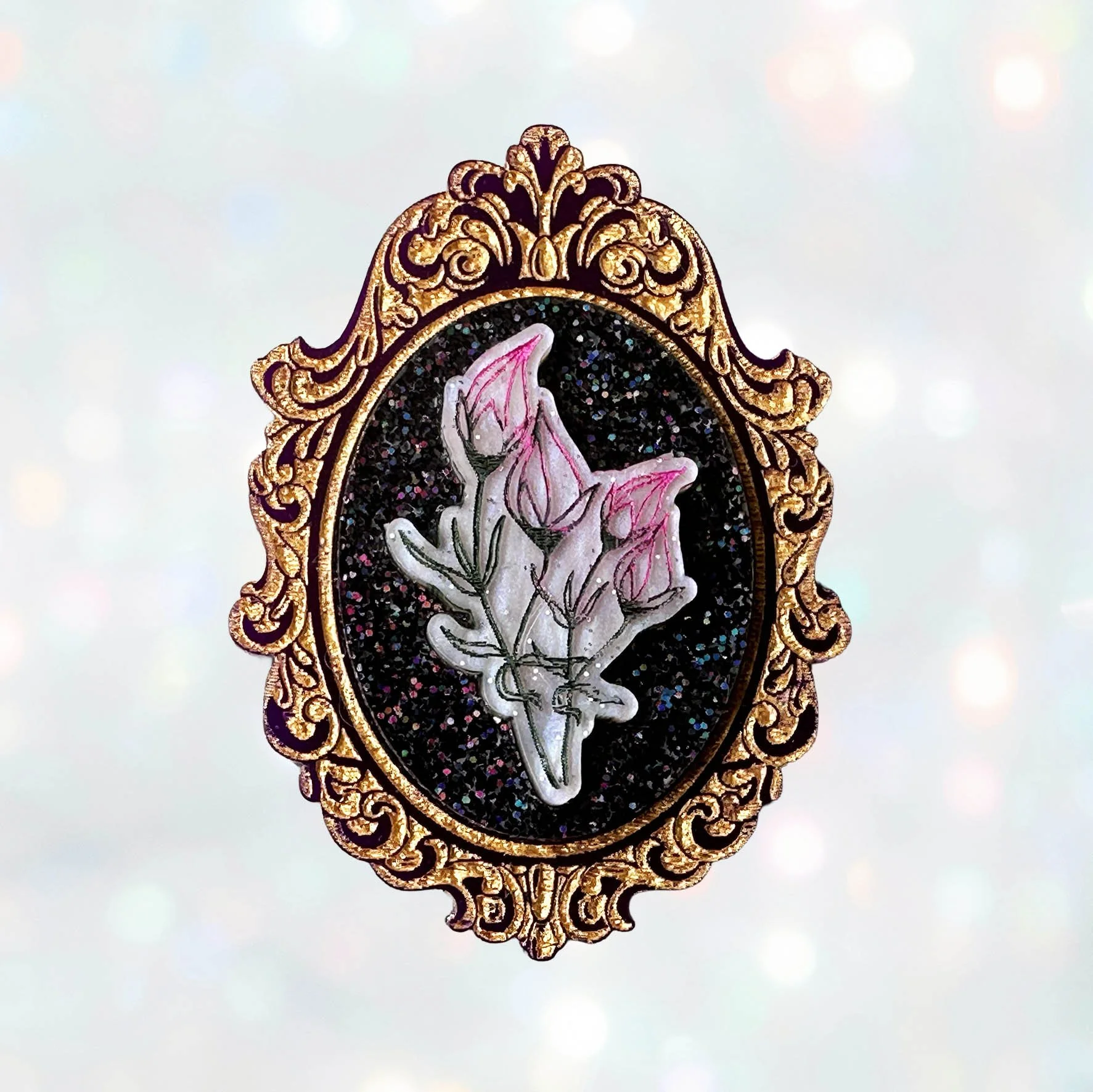 A laser cut acrylic cameo style brooch featuring a bunch of flowers within a purple and gold frame