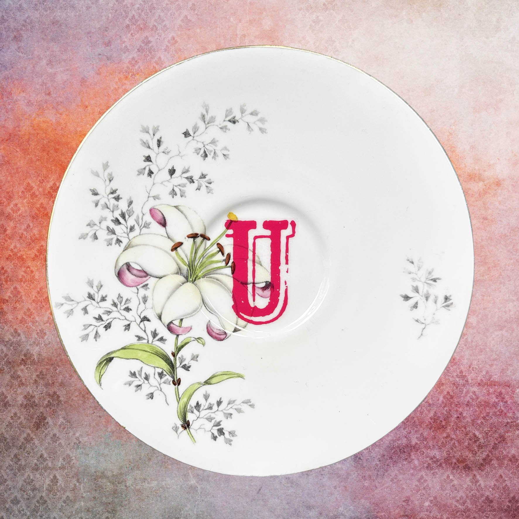 A vintage saucer with pink flowers and a pink letter “u”