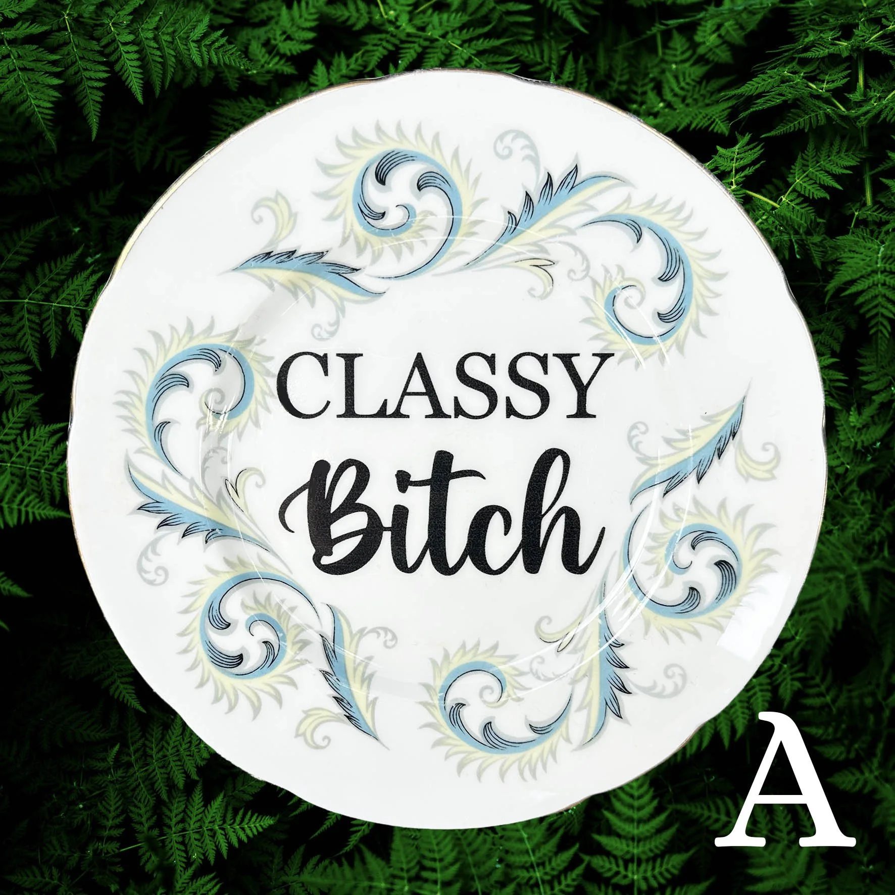 A vintage decorative wall plate with the words "classy bitch" in black writing