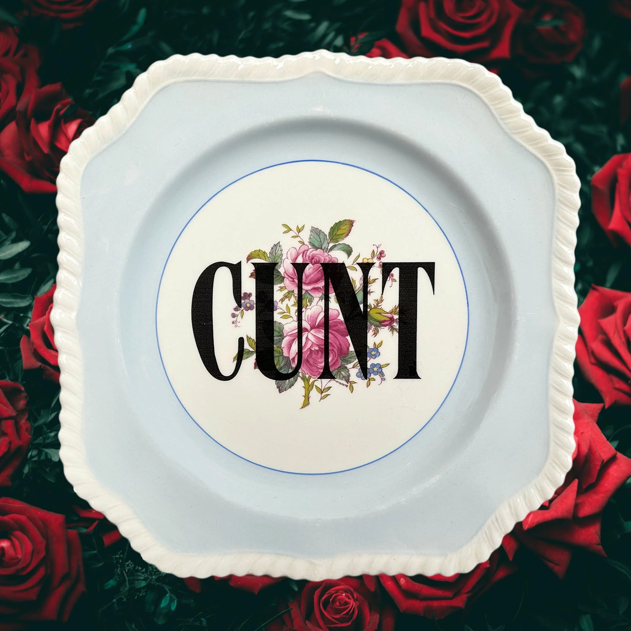 A vintage floral plate with a blue border and the words “cunt” in black lettering