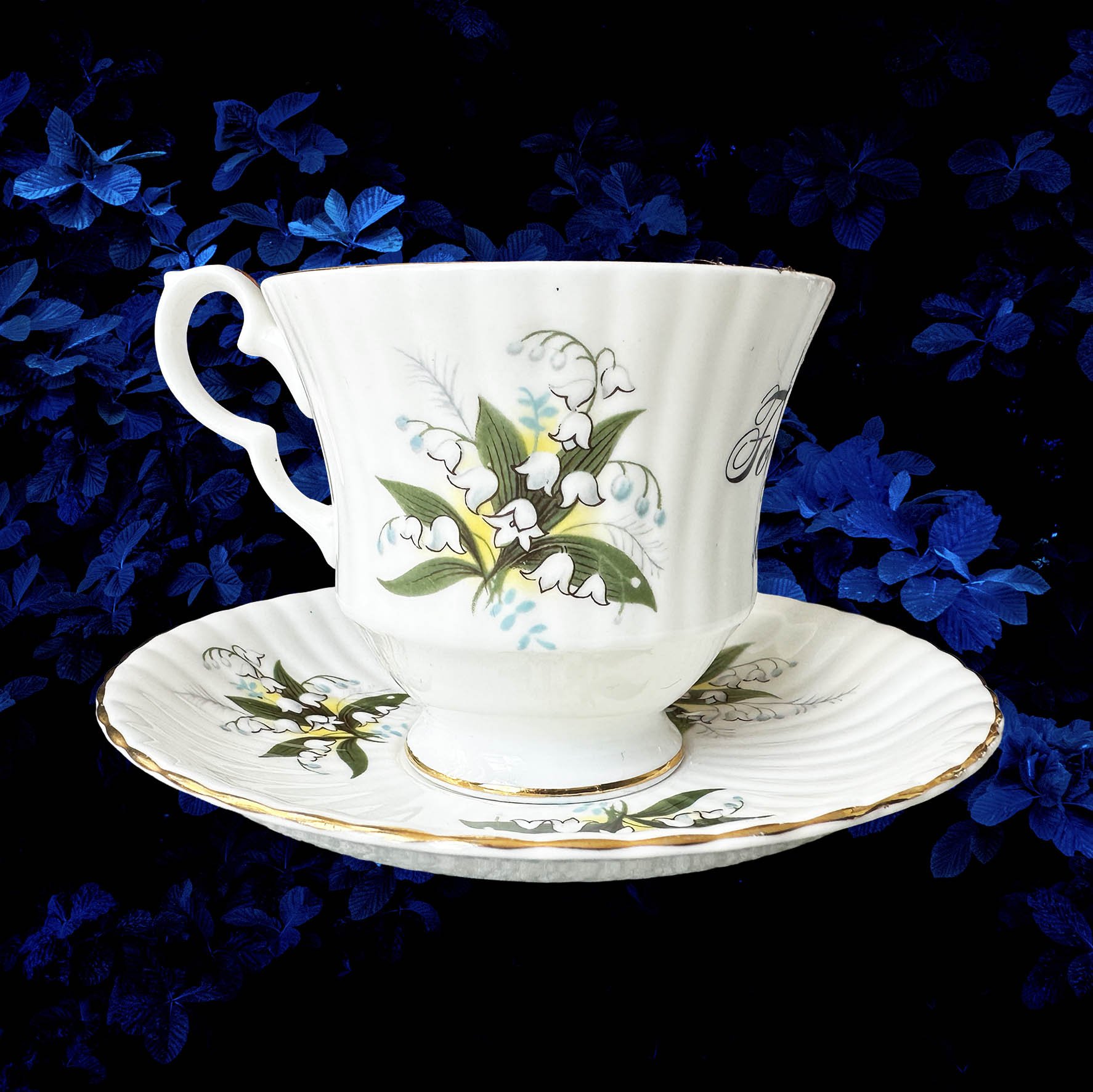 A vintage tea cup with a white and green floral design and a quote “for fuck’s sake” in black writing
