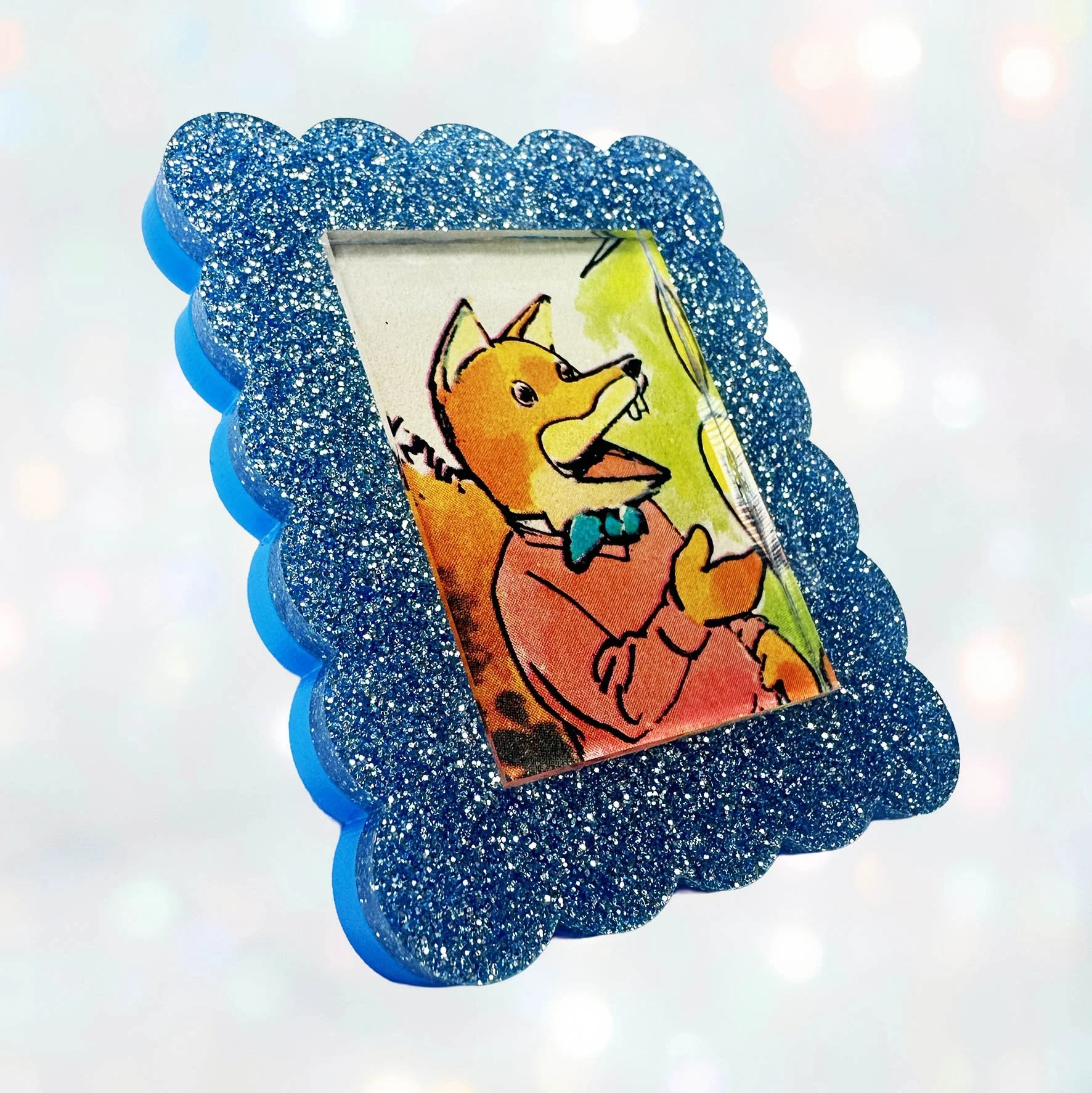 A light blue glitter acrylic brooch featuring a picture of Basil Brush