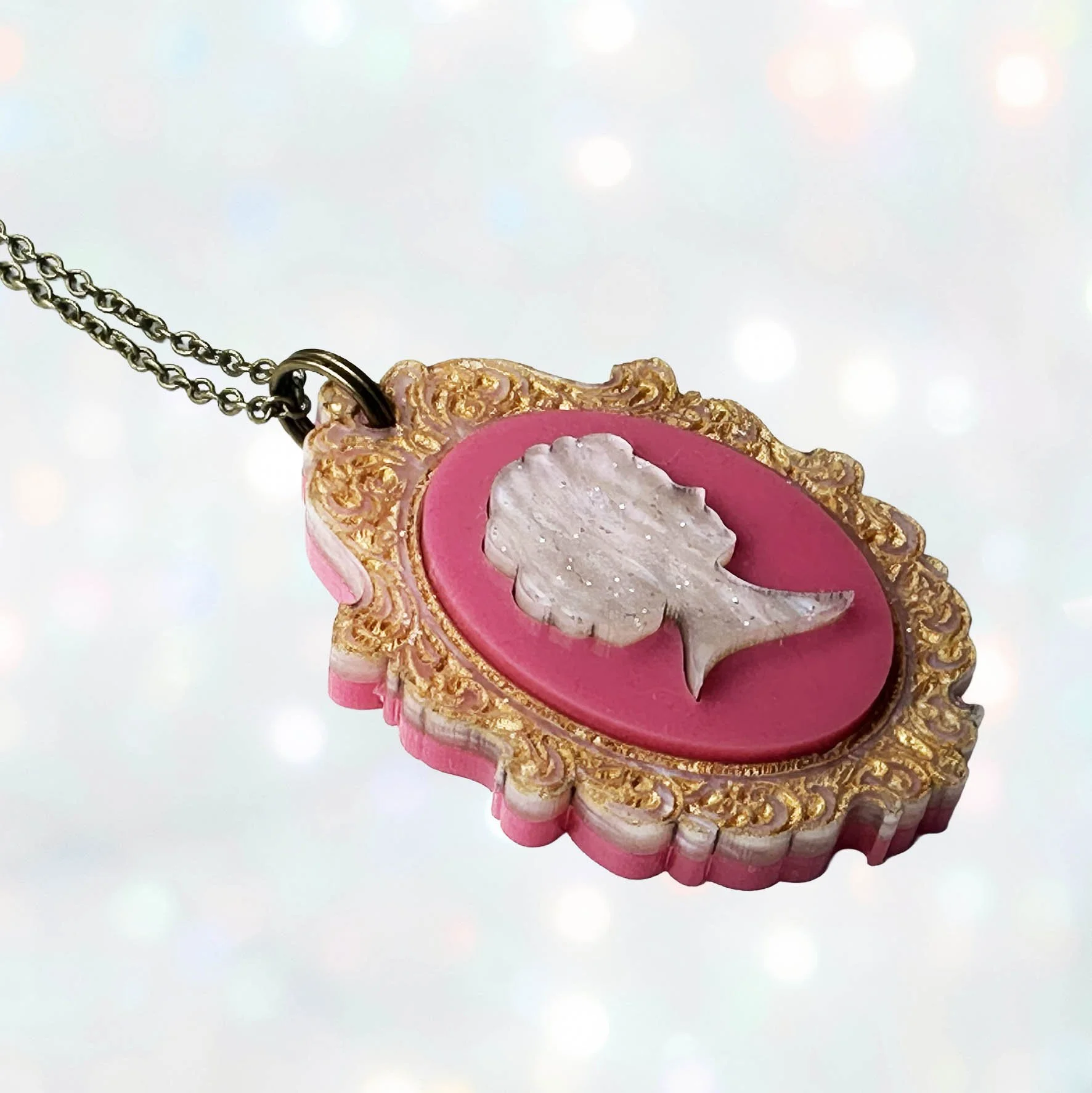 A laser cut pink and gold acrylic cameo style necklace featuring a silhouette