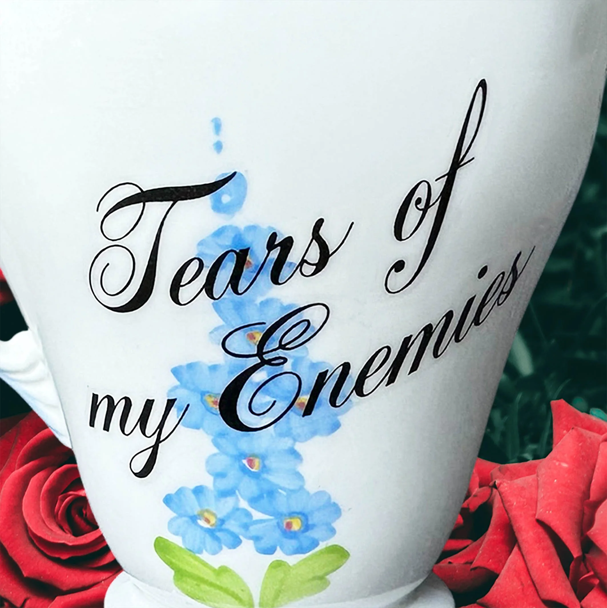 A vintage milk jug with blue flowers, the words “tears of my enemies” in black cursive writing