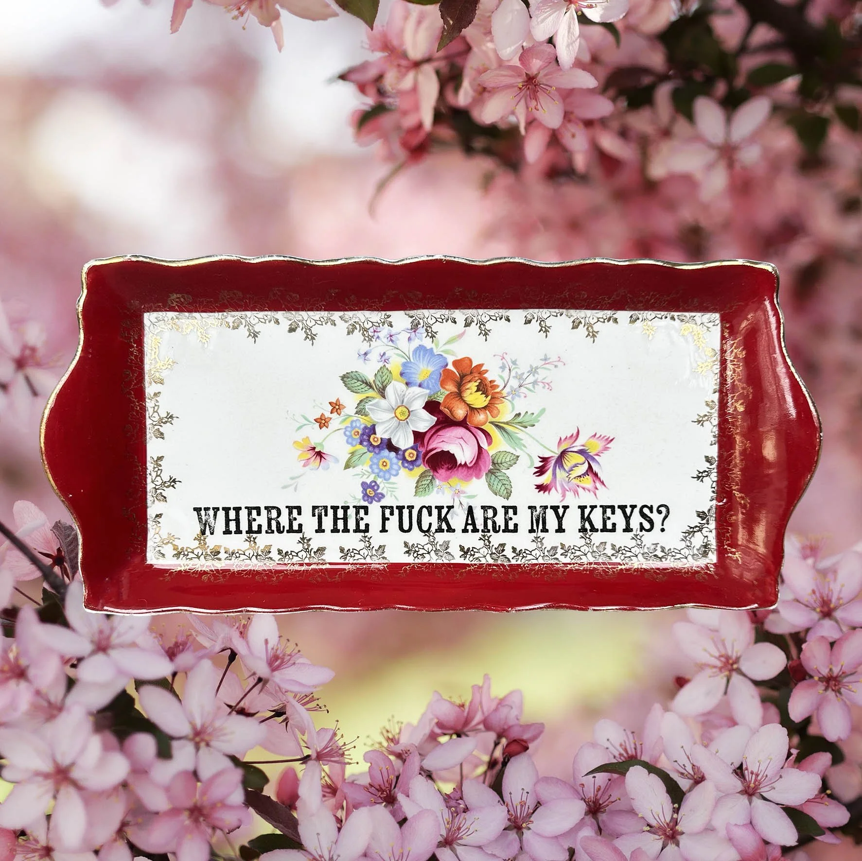 A vintage trinket dish with a red border and a floral design with the words “where the fuck are my keys?”