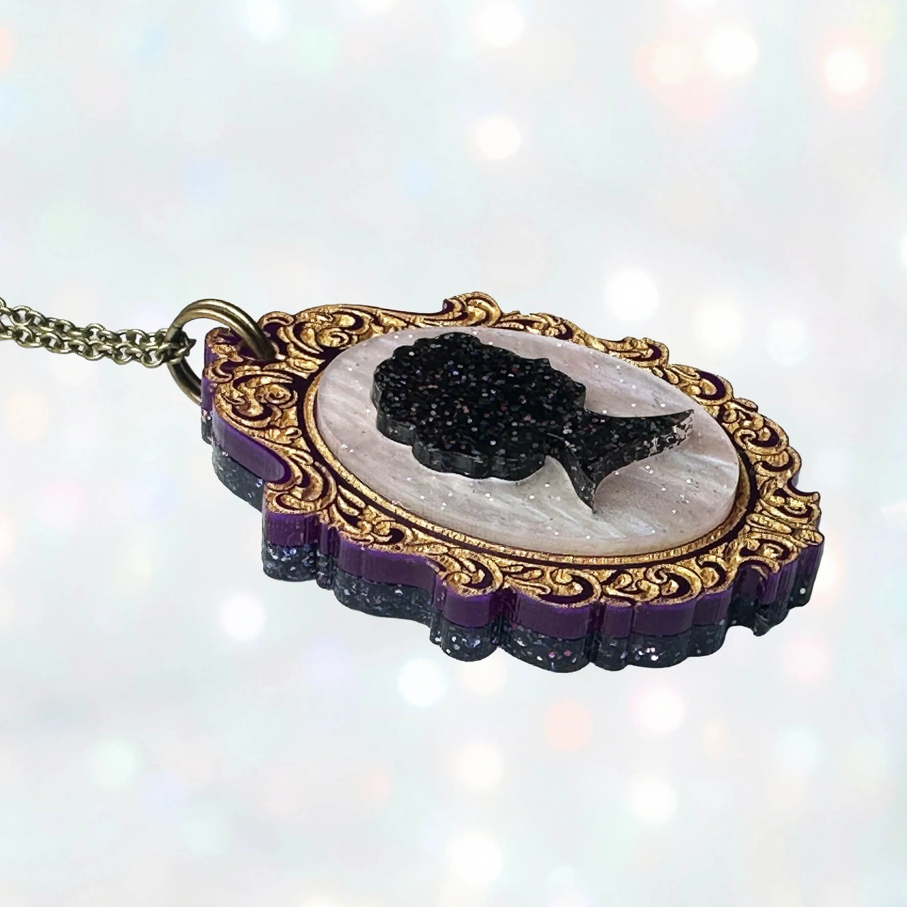 A purple, pink and gold laser cut acrylic cameo style necklace featuring a silhouette