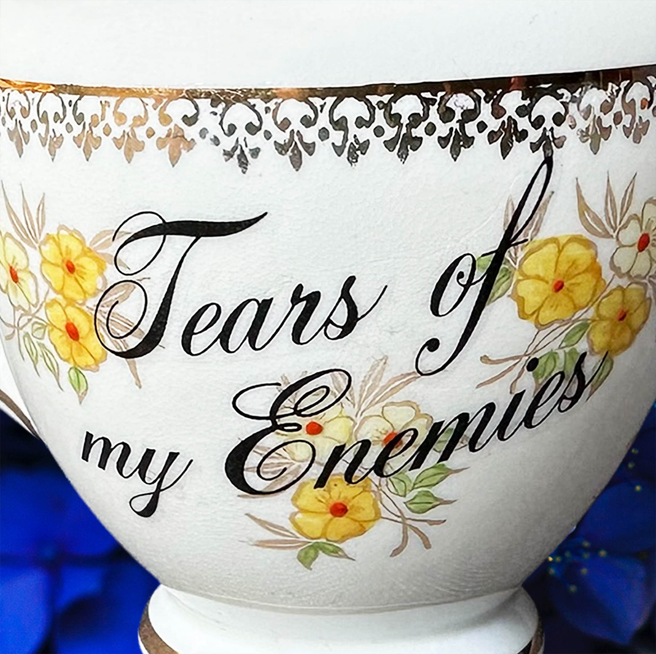A cream vintage milk jug with yellow flowers, the words “tears of my enemies” in black cursive writing