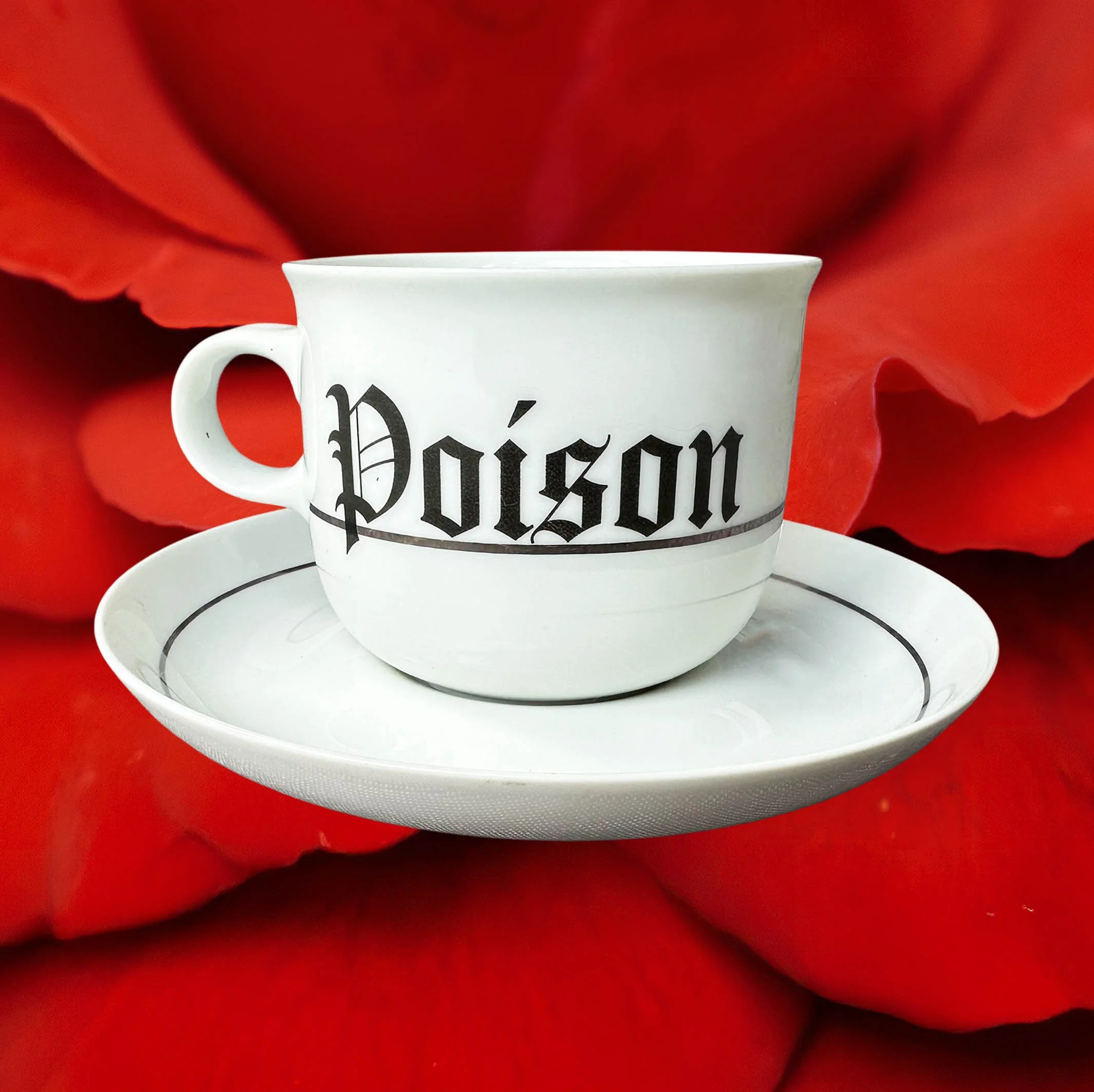 A vintage white tea cup and saucer with a silver band, with the words “Poison” in black gothic style lettering