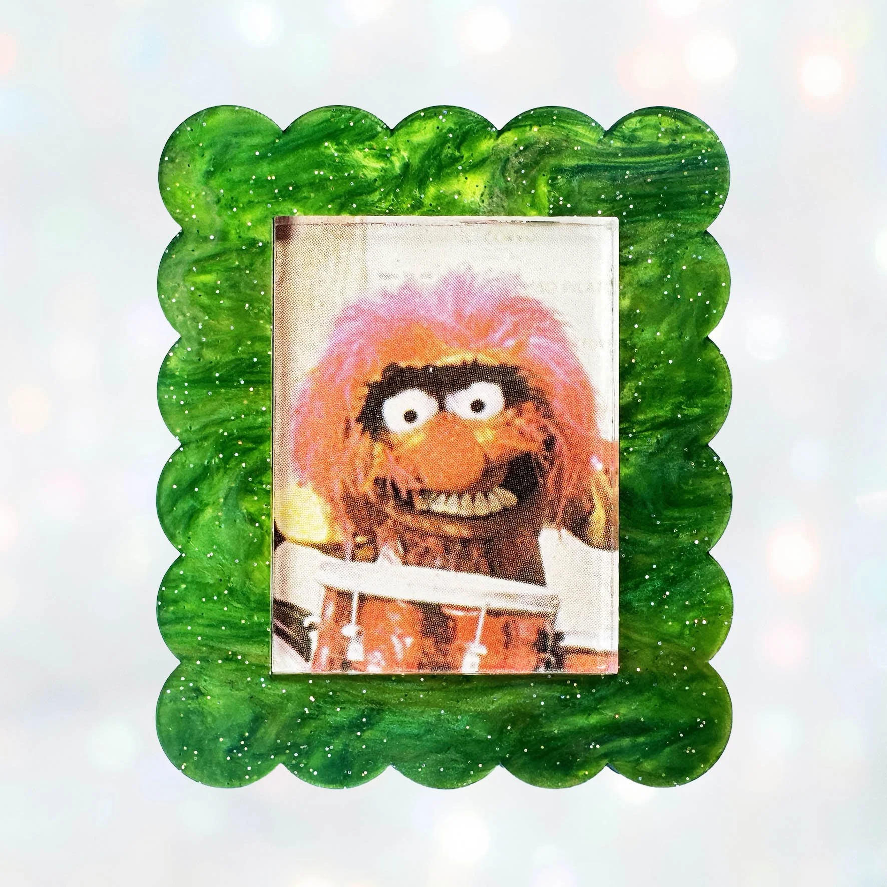 A green glitter acrylic brooch featuring a picture of Animal from The Muppet Show