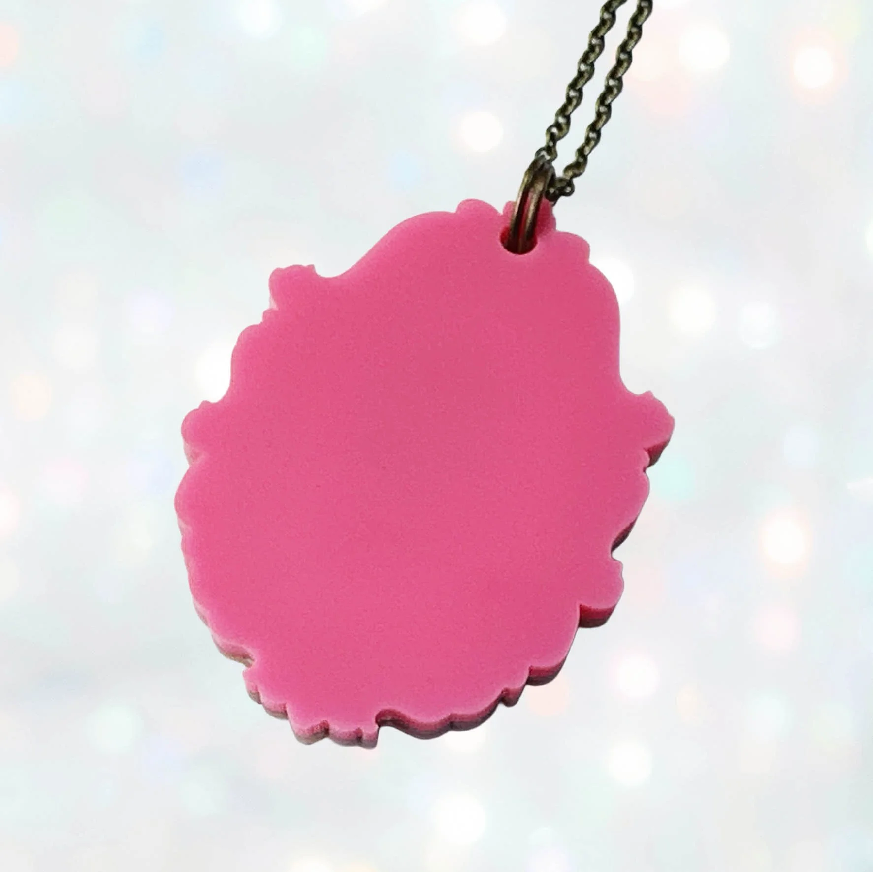 A pink, gold and black glitter laser cut acrylic cameo style necklace featuring a silhouette