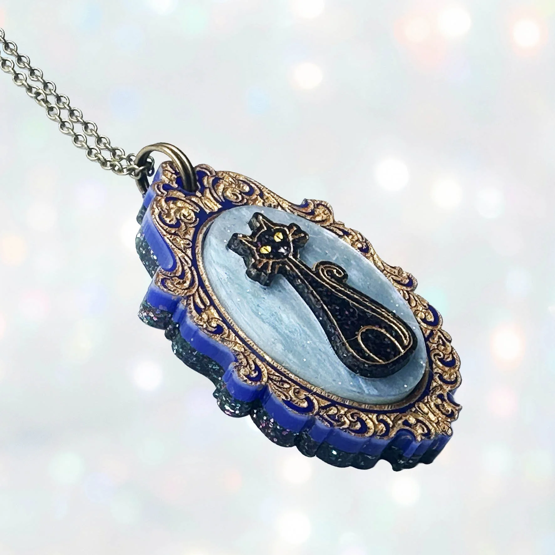 A laser cut acrylic cameo style necklace featuring a black cat inside inside a gold frame