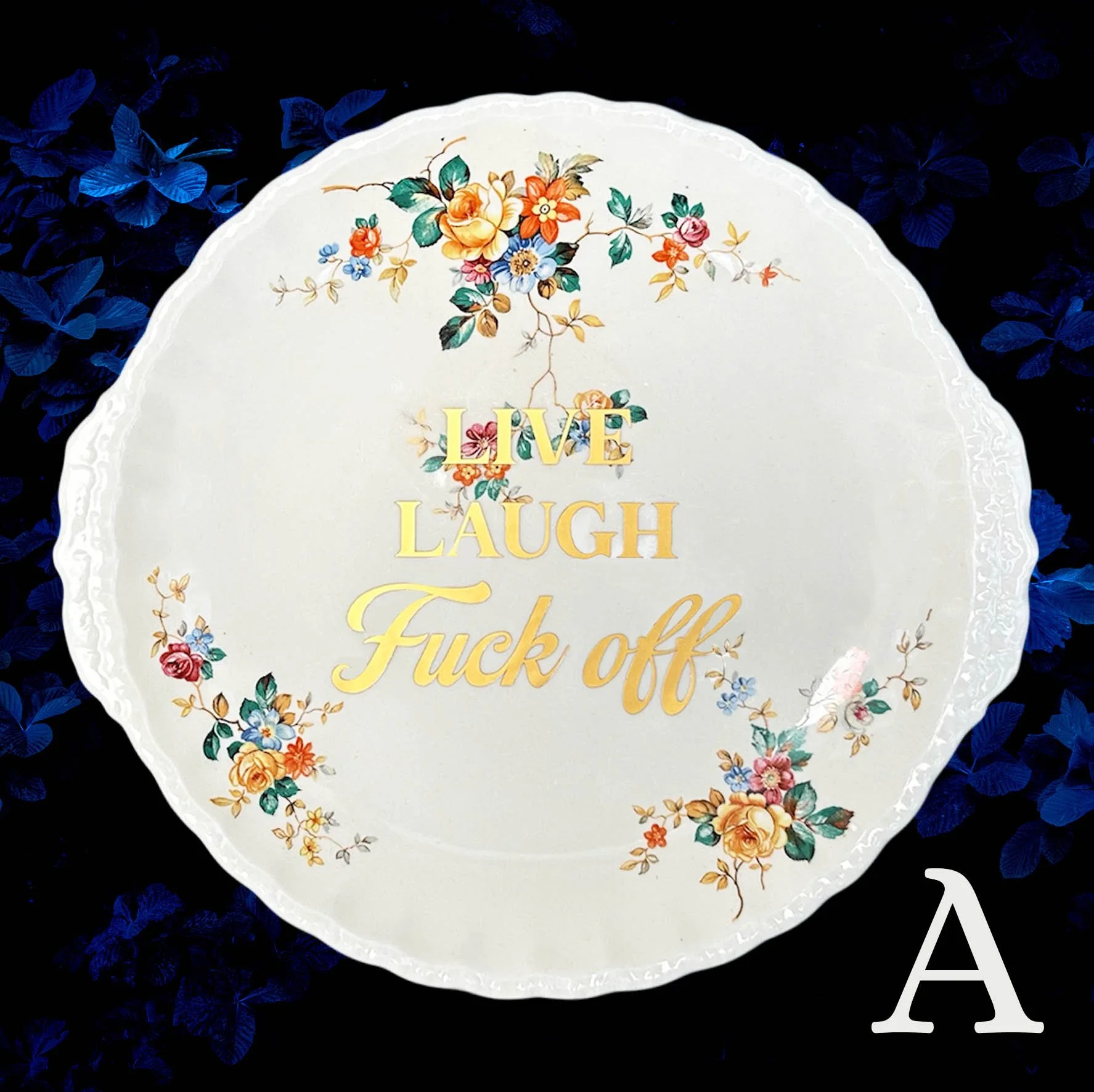 A vintage plate with a yellow, orange and red floral design with the words “live laugh fuck off” in gold writing
