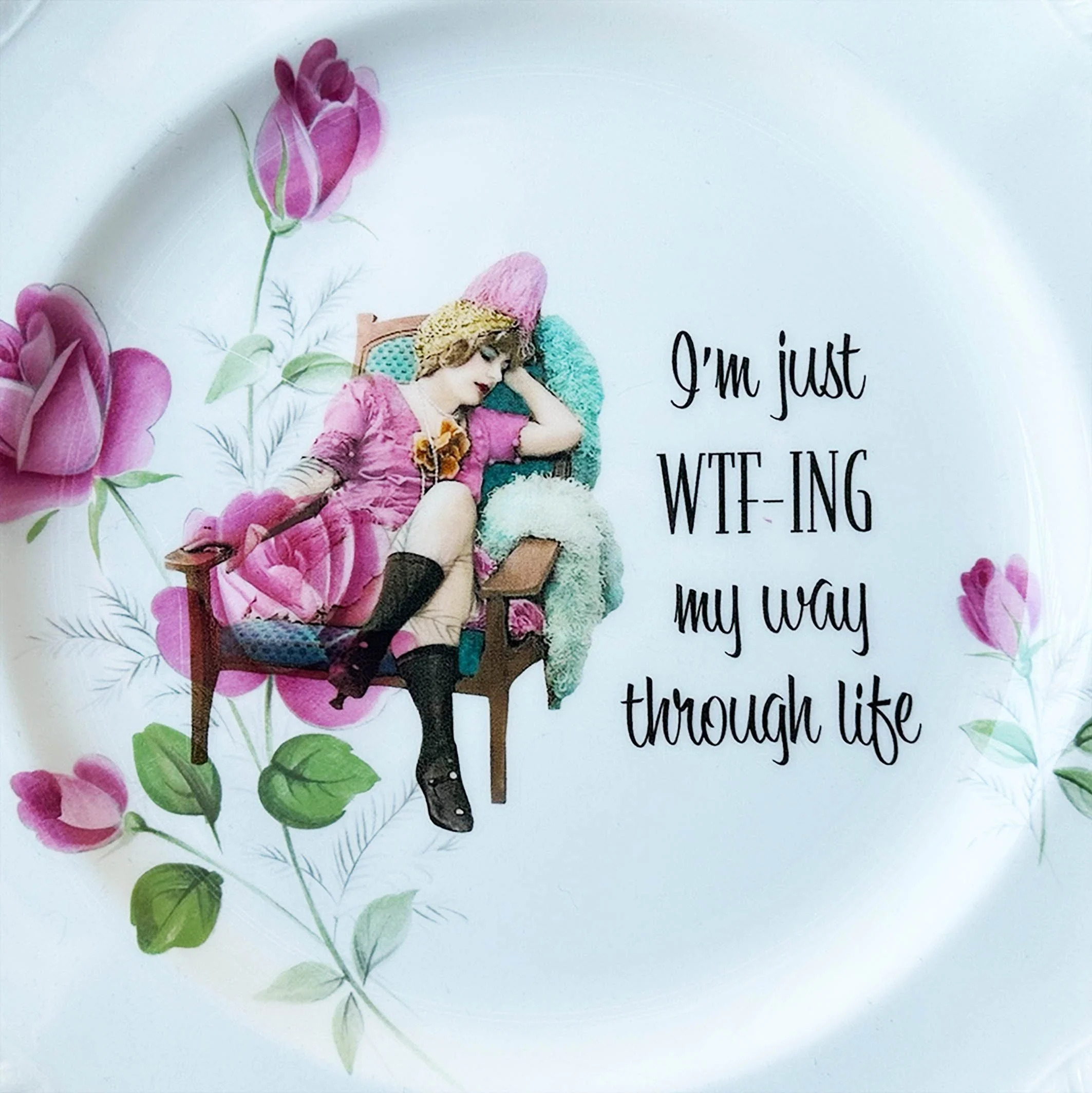 A vintage wall plate with pink roses and the words "I'm just WTF-ING my way through life" in black writing