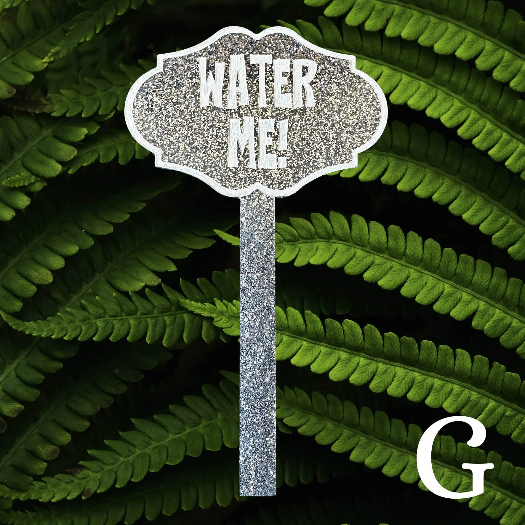 G, silver glitter planter stick label with the words “water me!” in white lettering