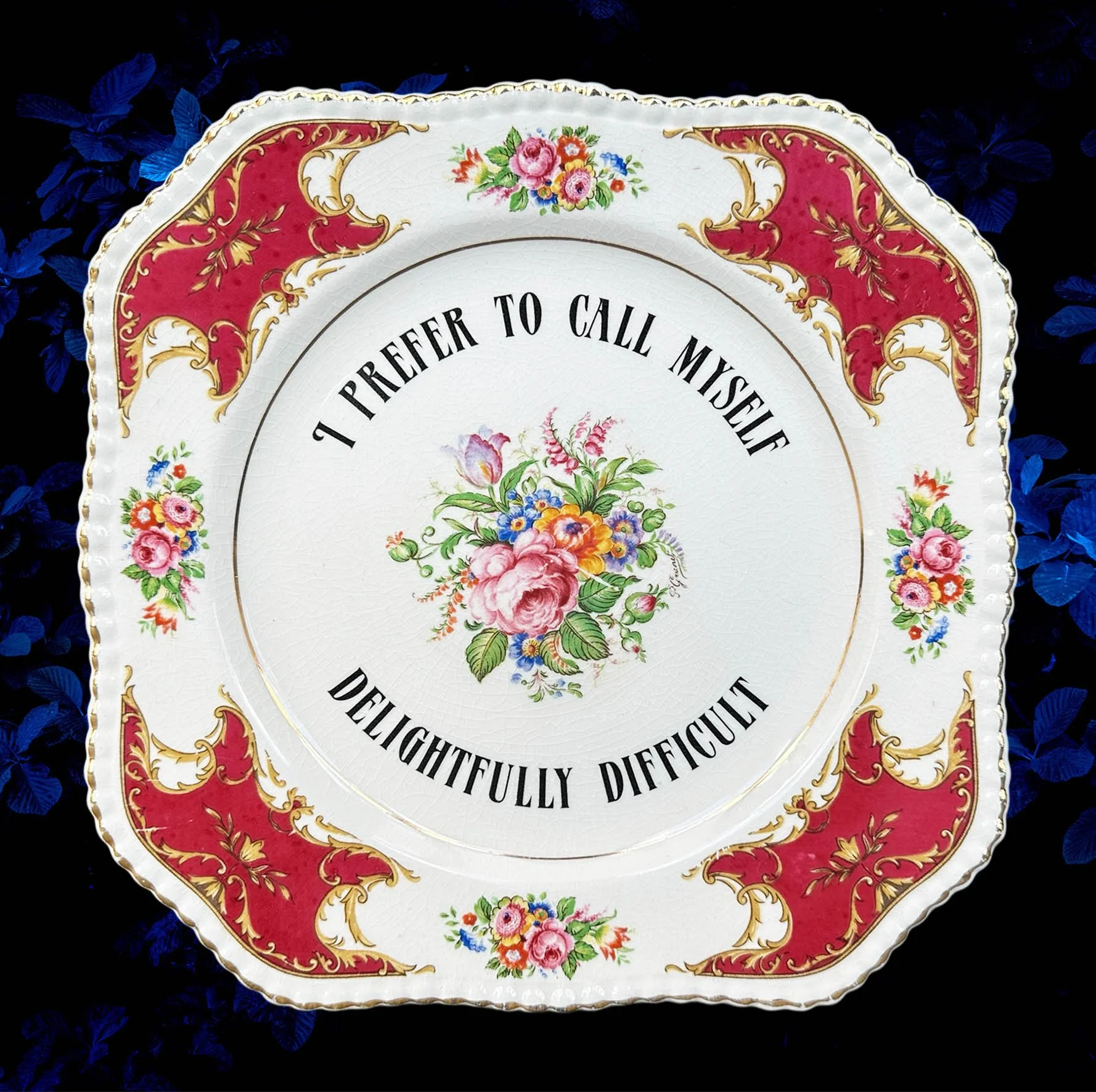 A vintage plate with the words “I prefer to call myself delightfully difficult” in black writing