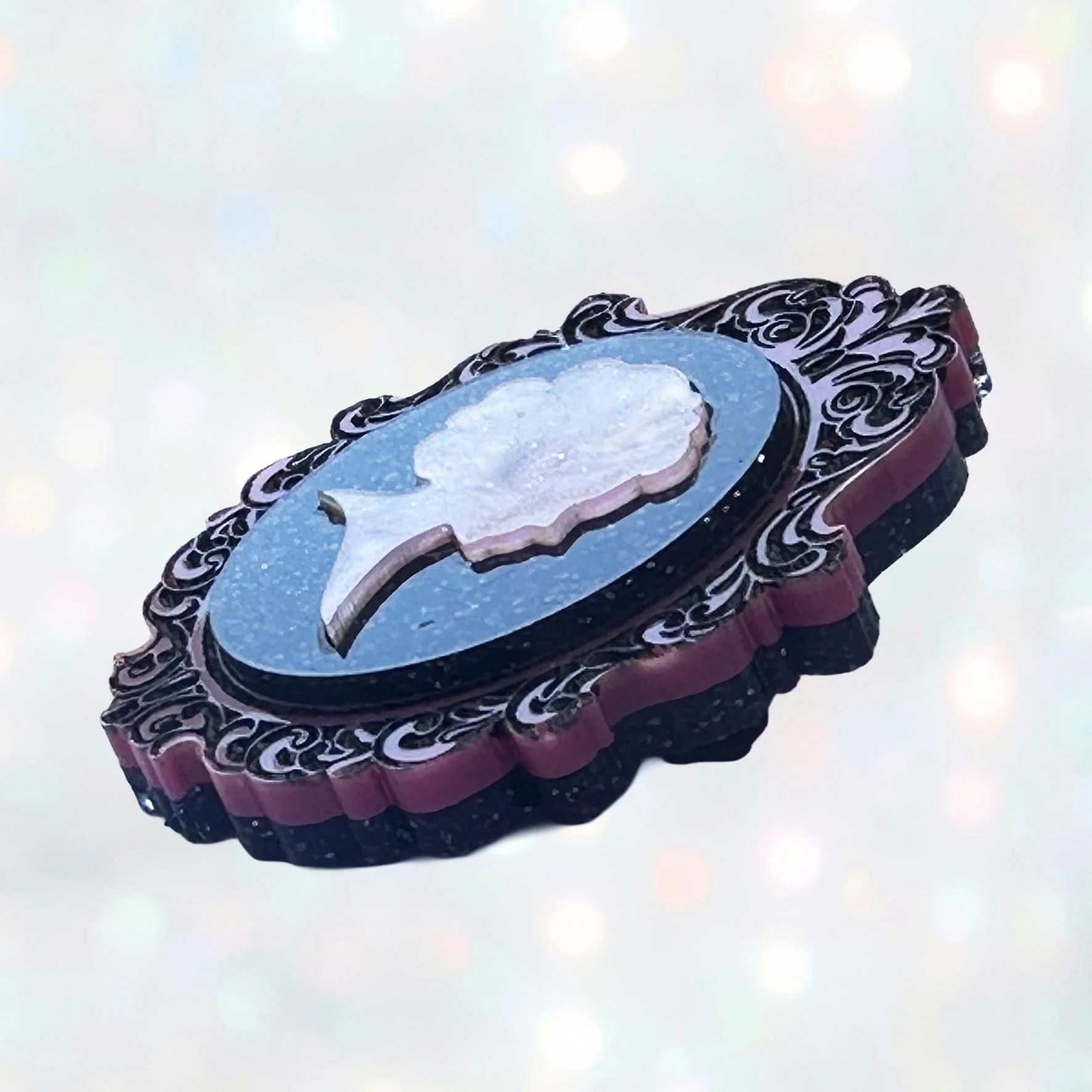 A pink and black glitter acrylic cameo style brooch featuring a silhouette