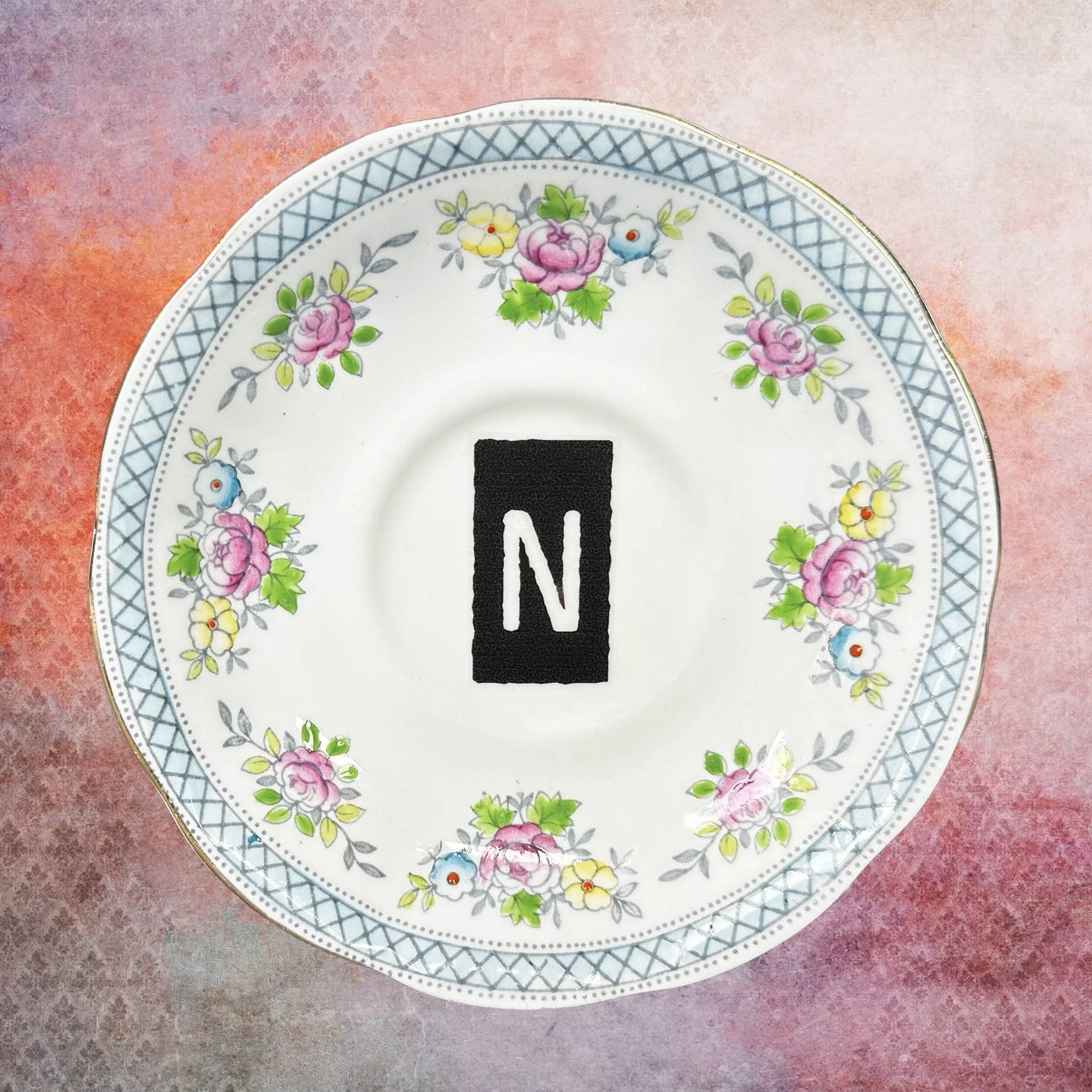A vintage saucer with blue and pink flowers and a letter “n”
