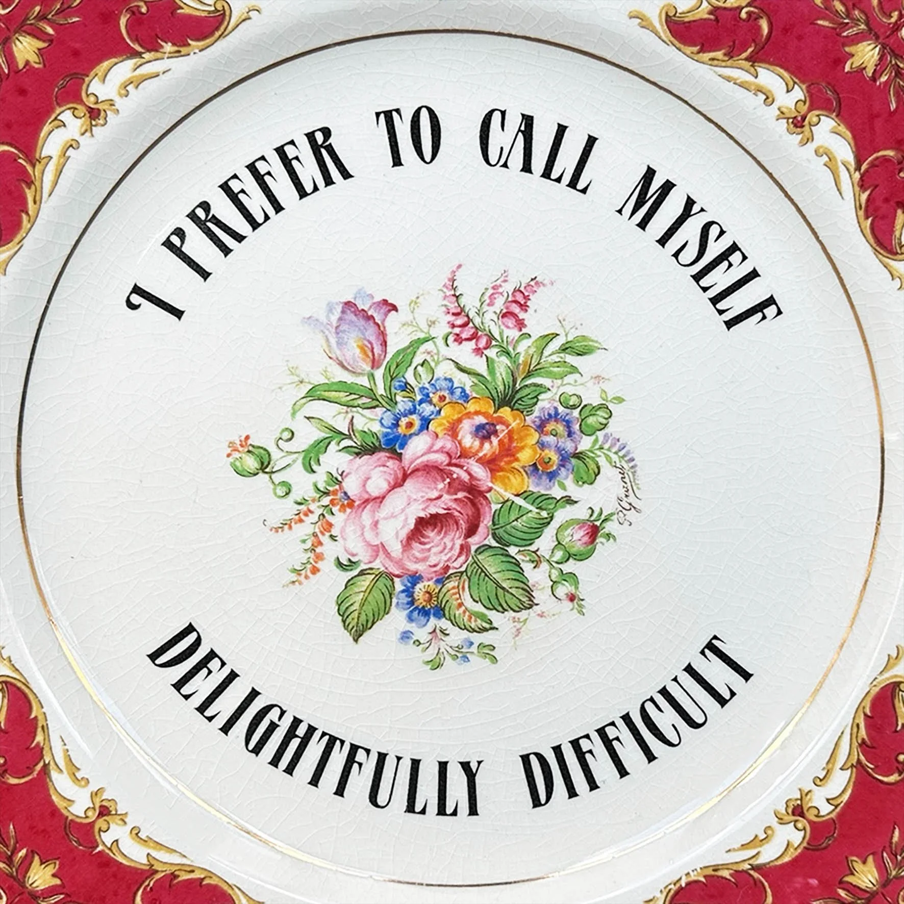 A vintage plate with the words “I prefer to call myself delightfully difficult” in black writing