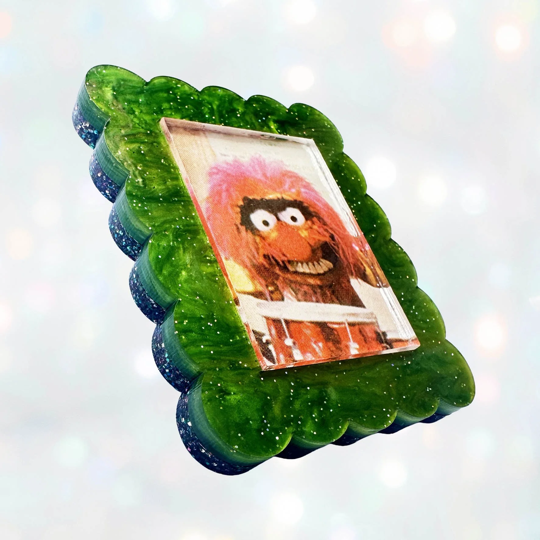 A green glitter acrylic brooch featuring a picture of Animal from The Muppet Show