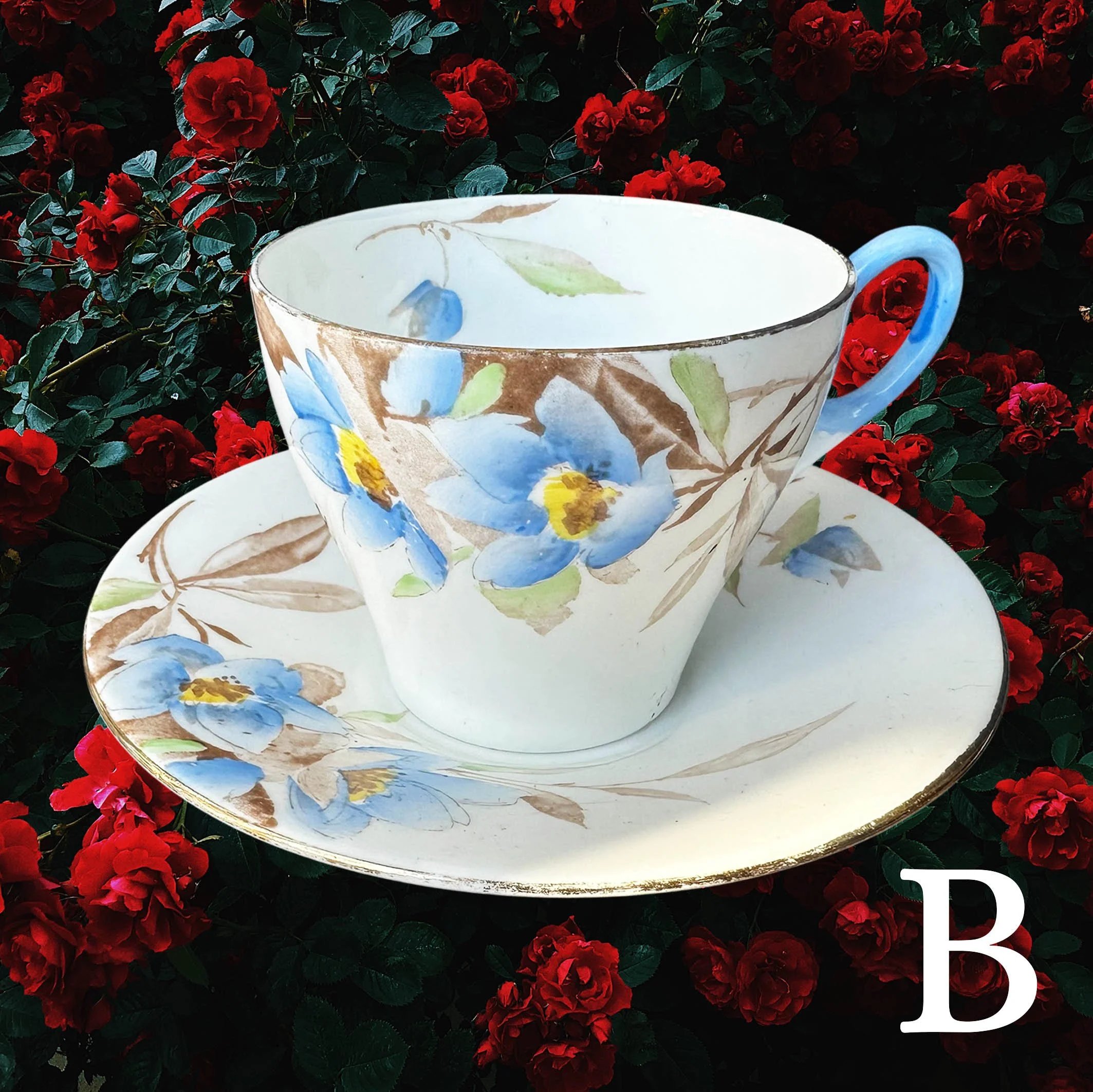 A vintage tea cup and saucer with a blue floral design and the words "let the good times be gin" in black cursive writing