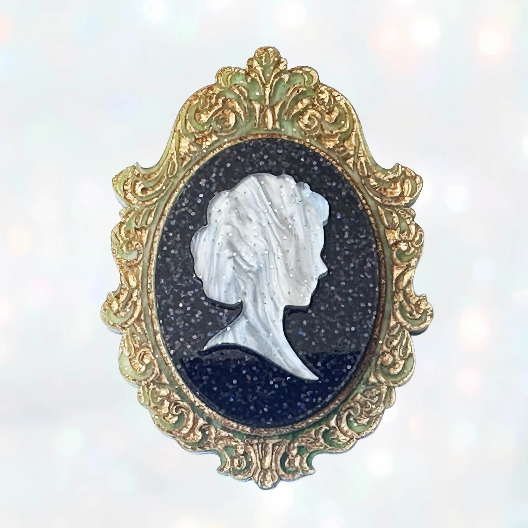 A laser cut green gold and black acrylic cameo style brooch featuring a silhouette
