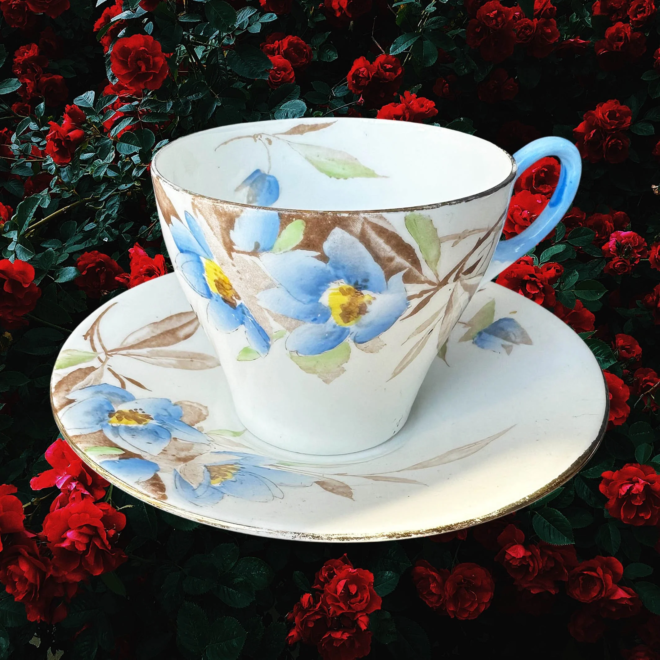 A vintage tea cup and saucer with a blue floral design and the words "let the good times be gin" in black cursive writing