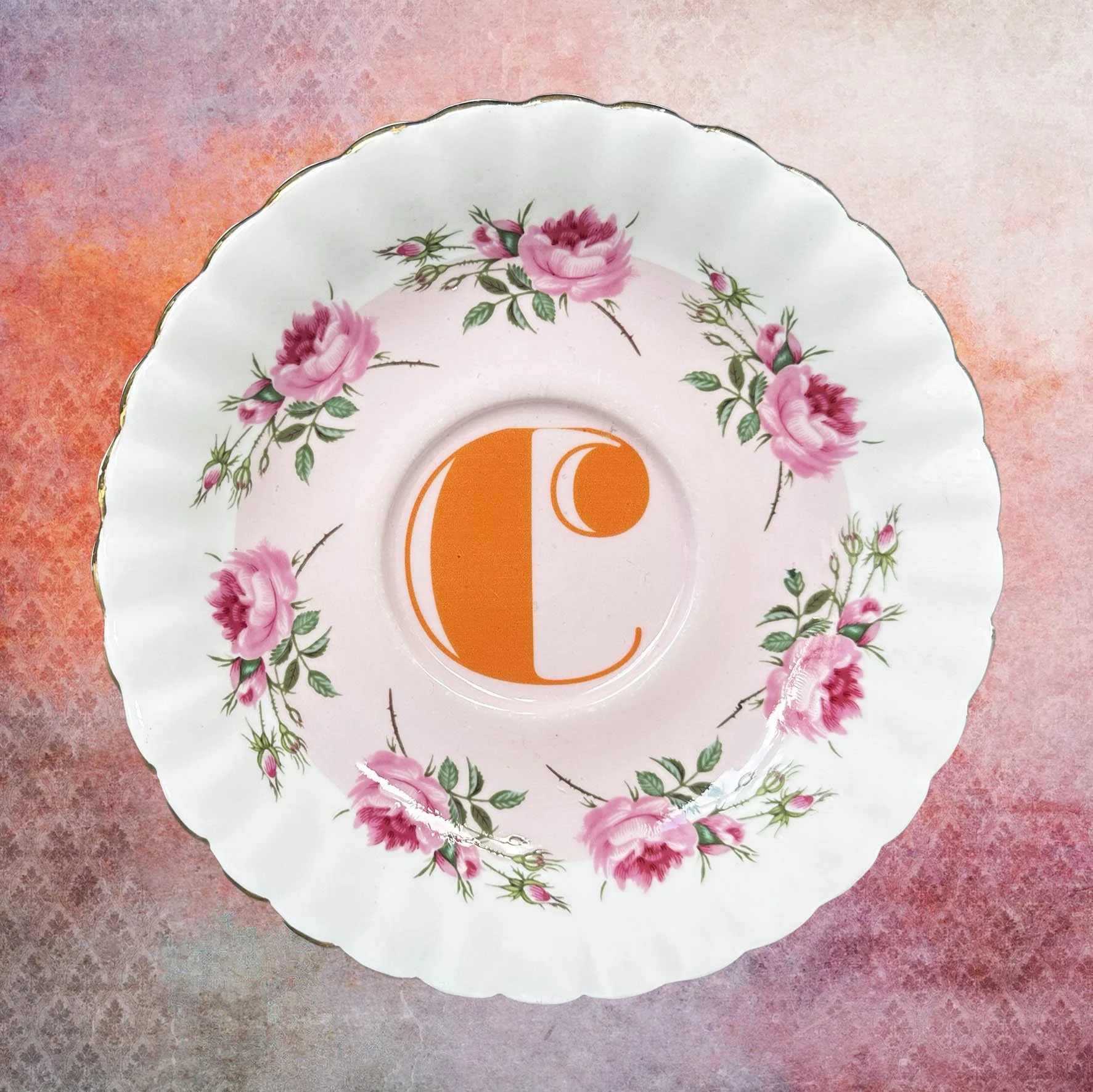 A vintage saucer with pink roses and an orange “c”