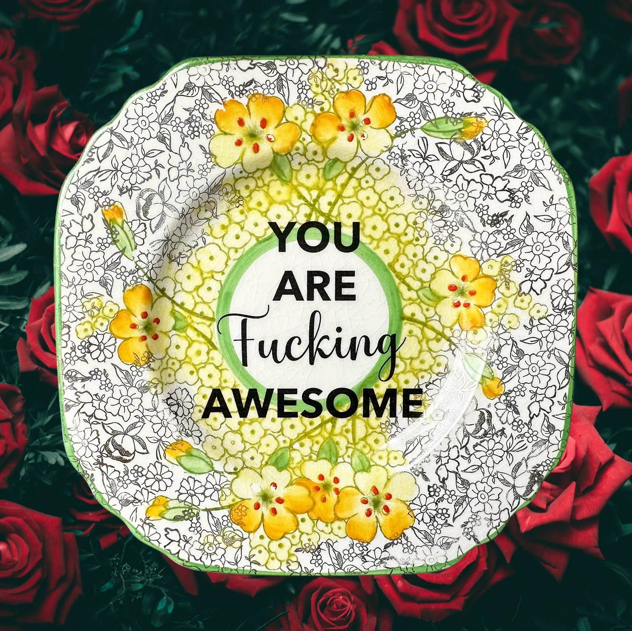 A vintage plate with a yellow and gold floral design and the words “you are fucking awesome” in black lettering