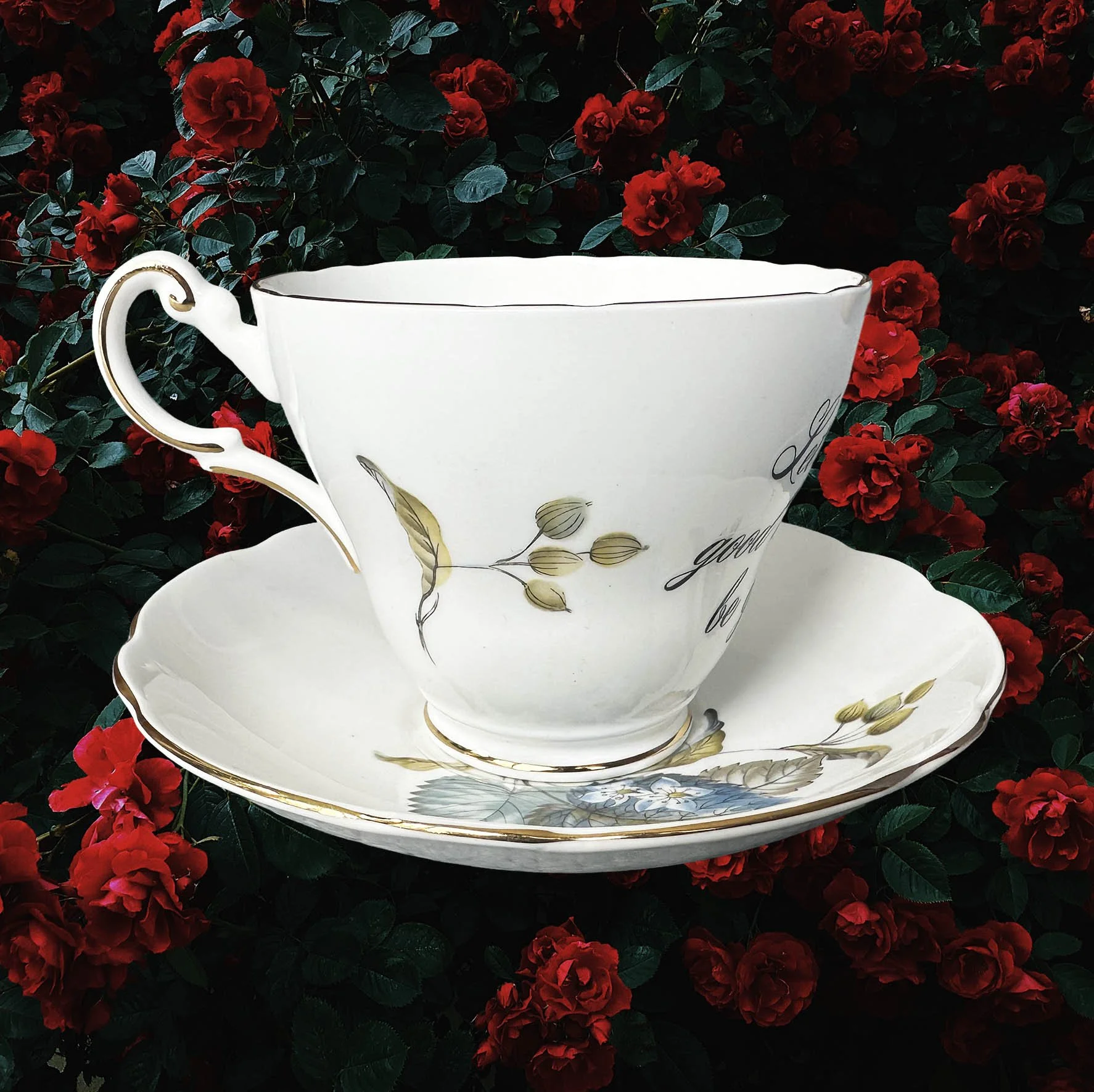 A vintage tea cup and saucer with a blue floral design and the words "let the good times be gin" in black cursive writing