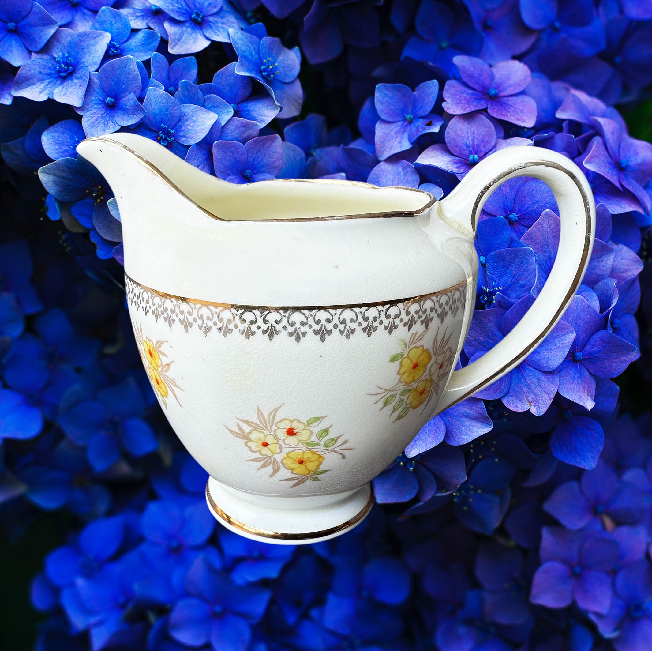 A cream vintage milk jug with yellow flowers, the words “tears of my enemies” in black cursive writing
