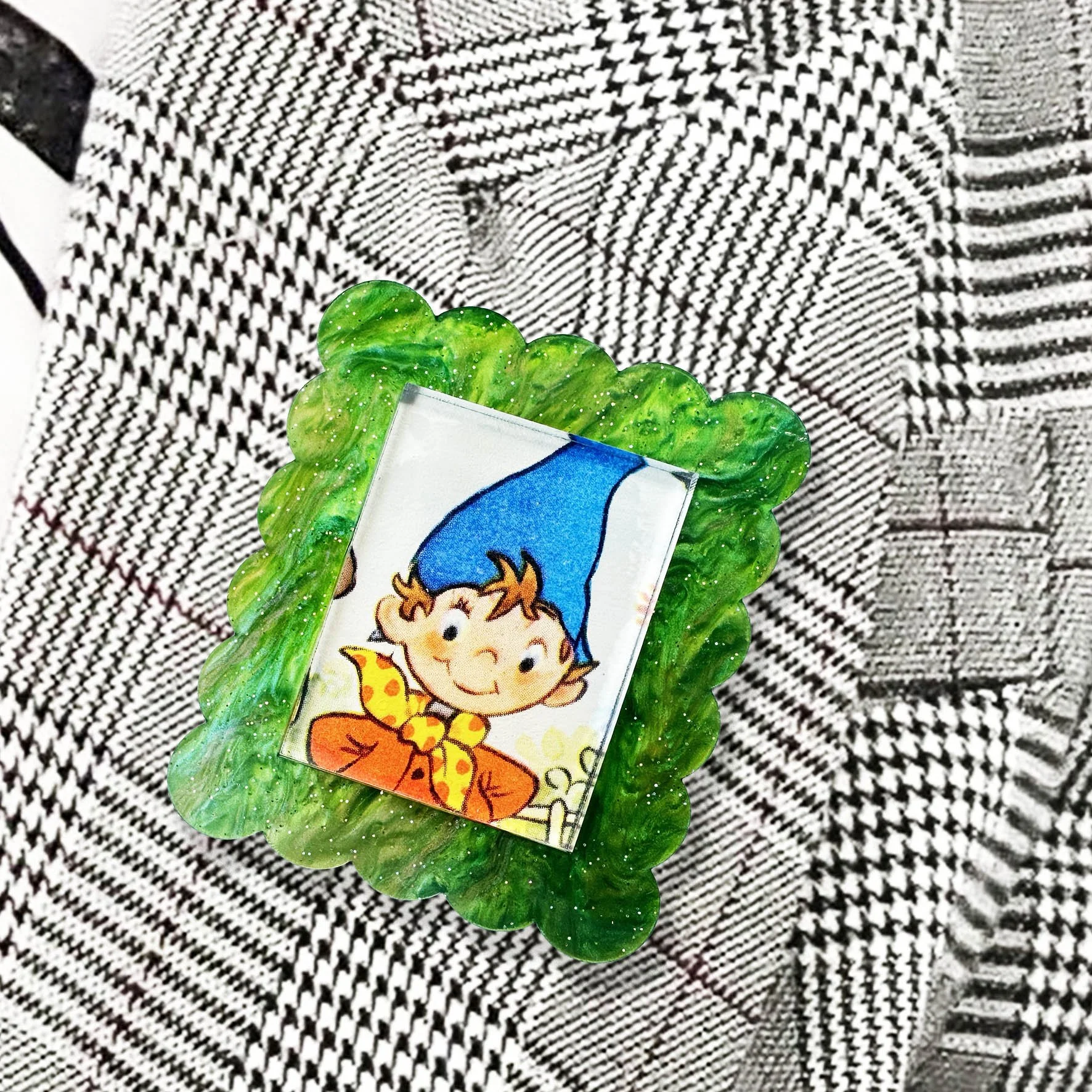 A green glitter acrylic brooch featuring a picture of Noddy