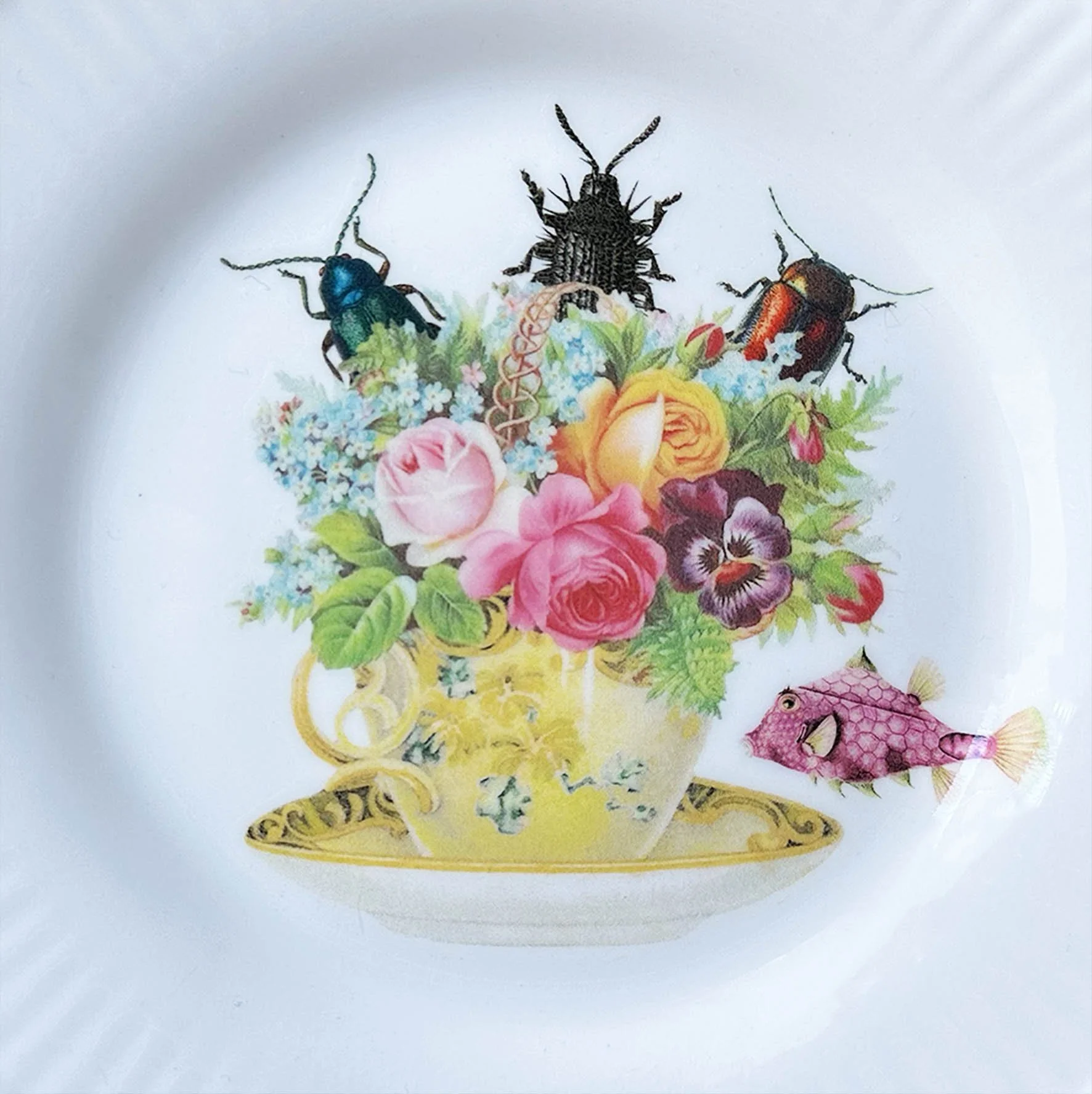 A vintage decorative plate with a picture of a tea cup full of flowers with bugs crawling out
