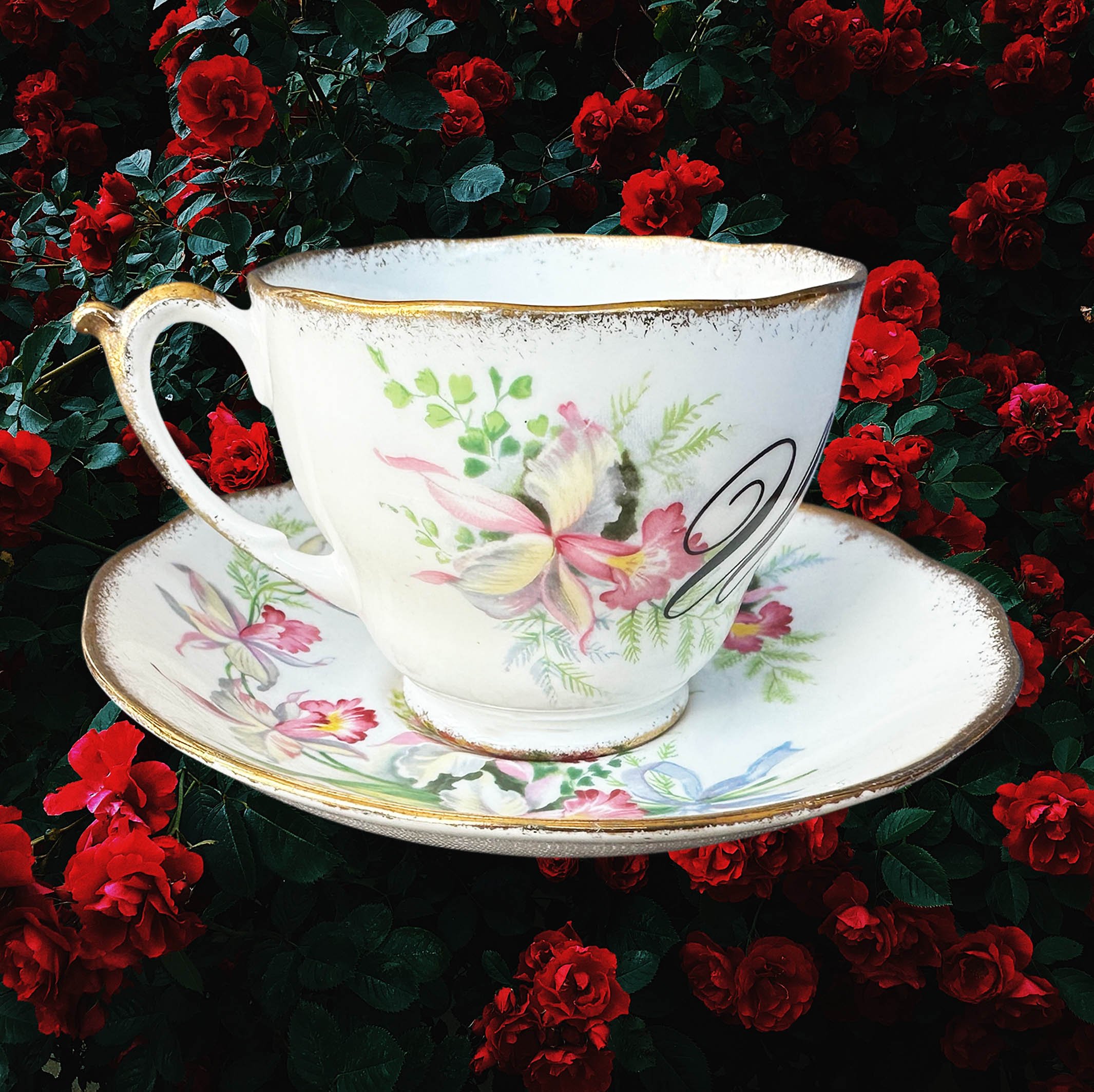 A vintage tea cup and saucer set with a pink floral design and the word "Whore" in black cursive writing
