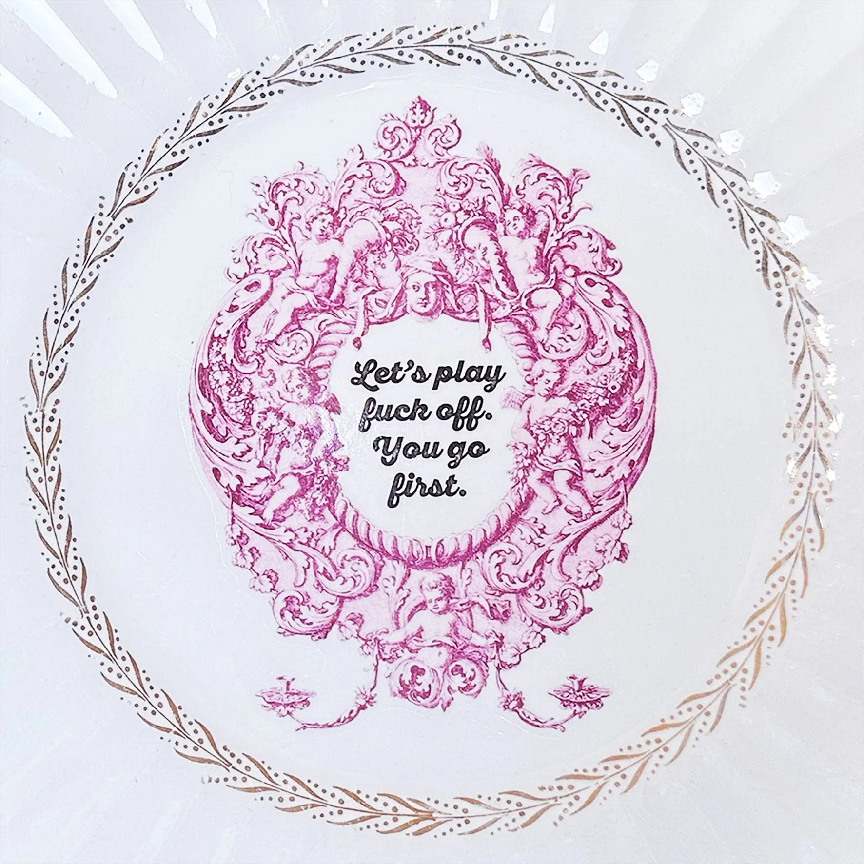 Plate A, a large vintage plate with an ornate pink frame with the words “let’s play fuck off. You go first”
