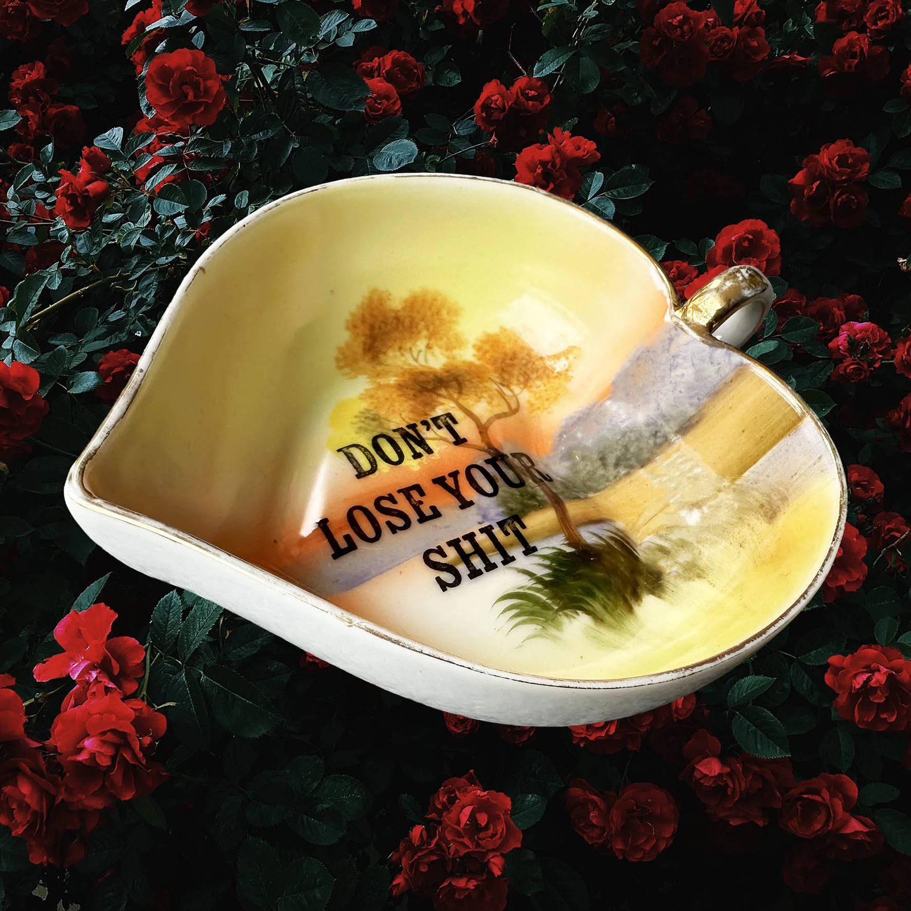 A heart shaped trinket dish with an orange, green and brown landscape design and the words “don’t lose your shit”