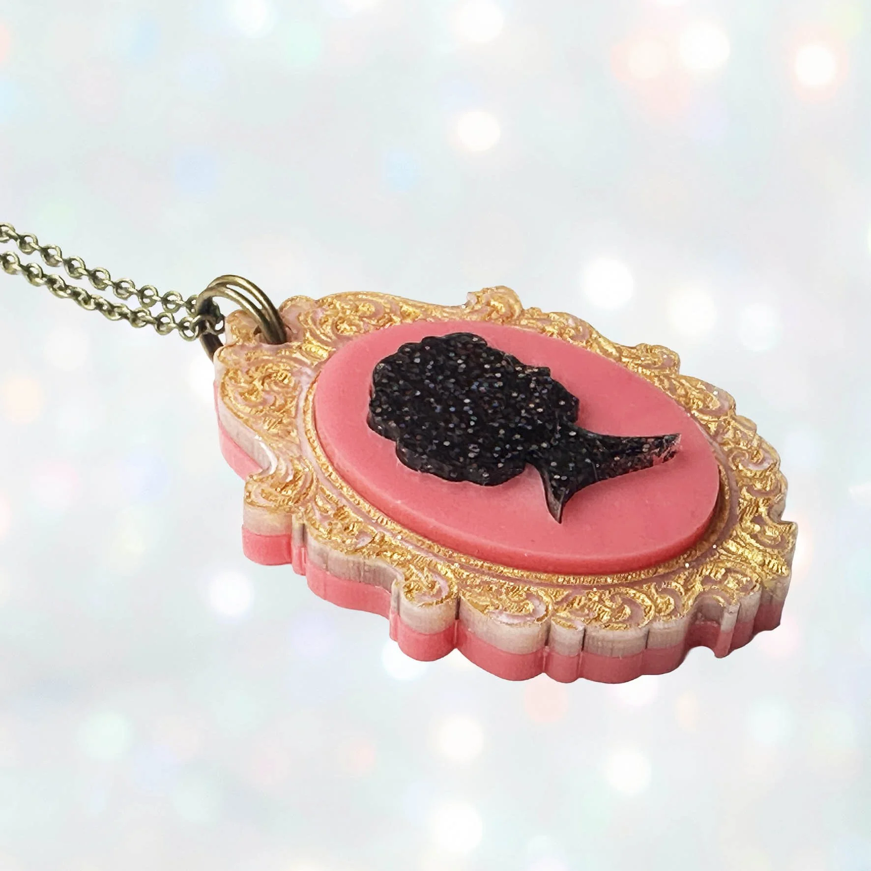 A pink, gold and black glitter laser cut acrylic cameo style necklace featuring a silhouette