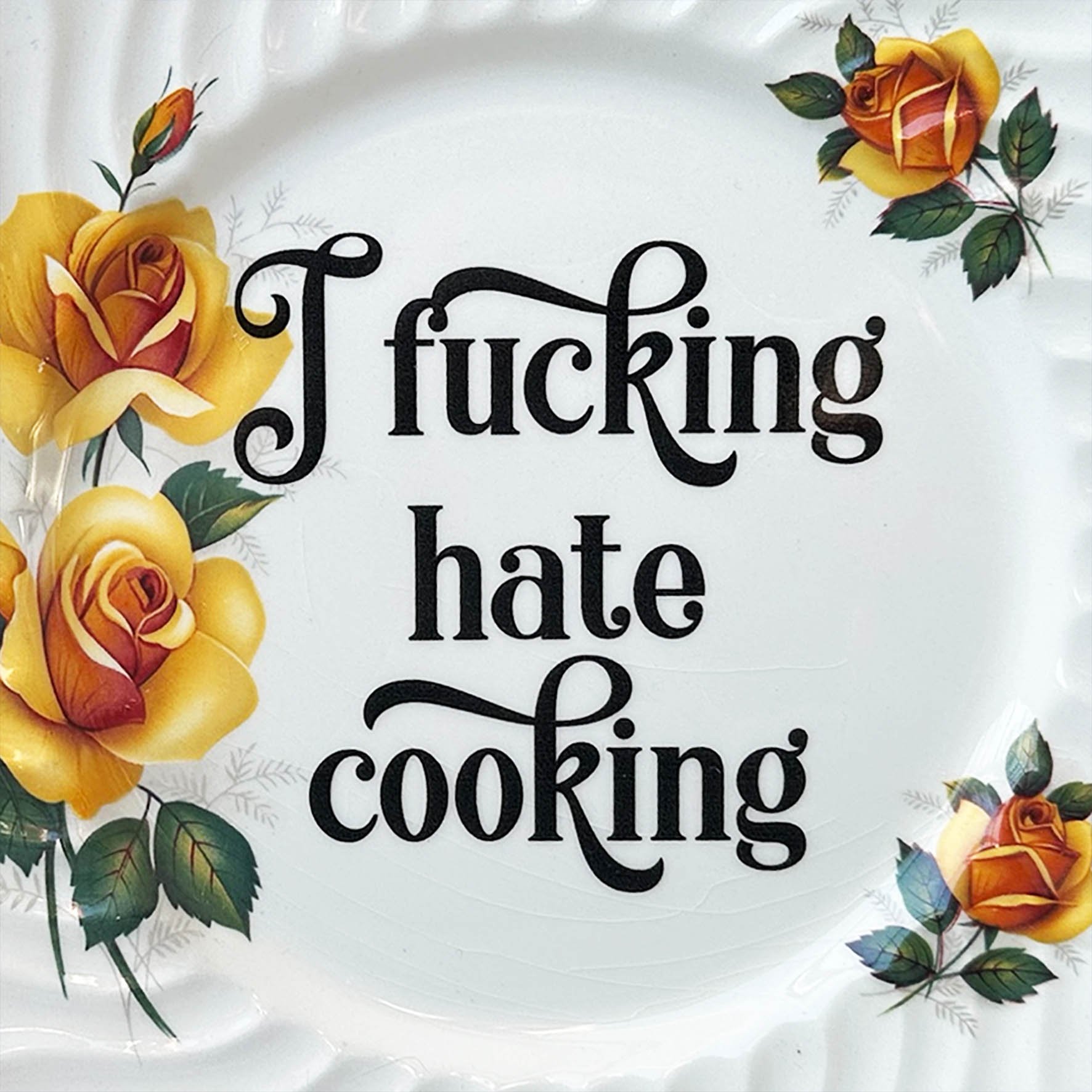 A vintage wall plate with yellow roses and the words “I fucking hate cooking” in black writing
