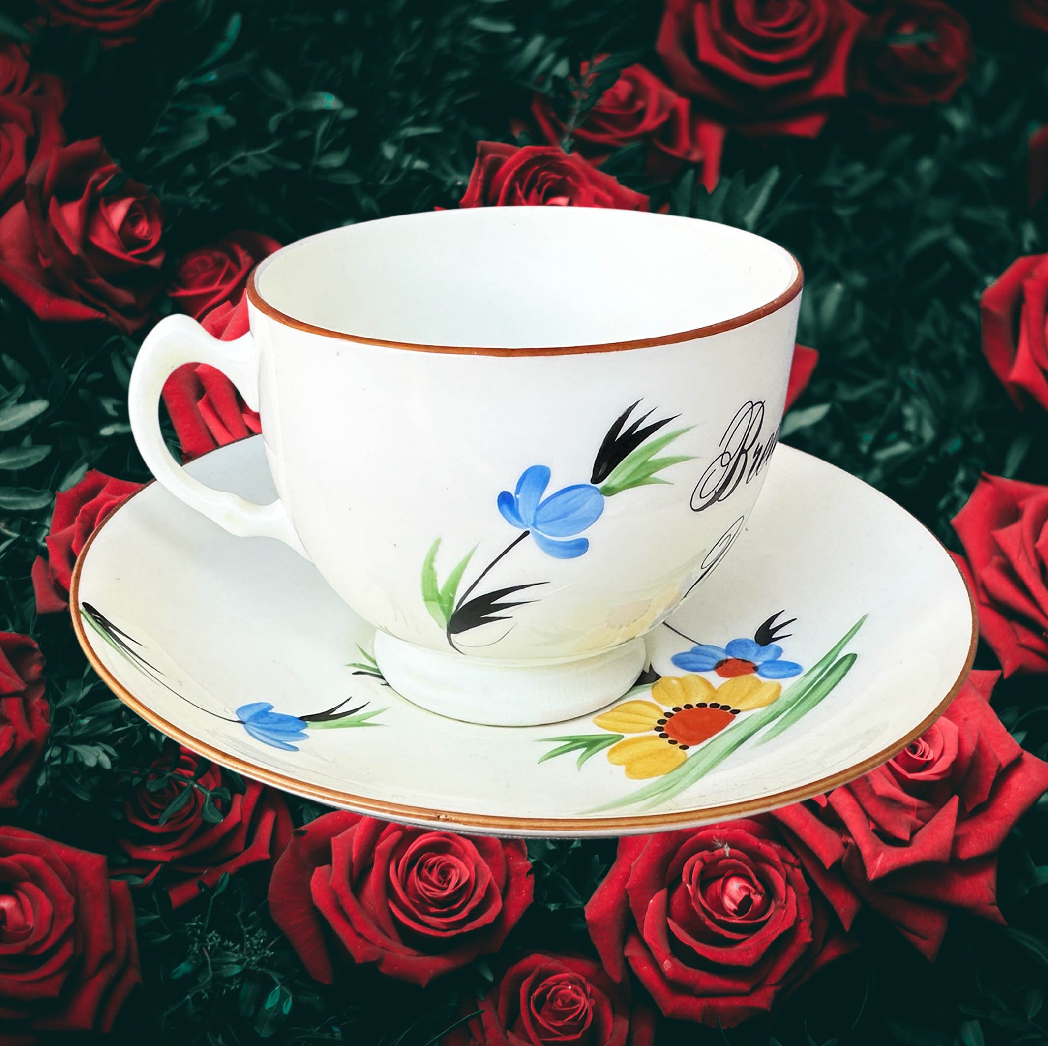 A vintage tea cup and saucer with a blue and green floral design, the words “breakfast wine” in black cursive writing
