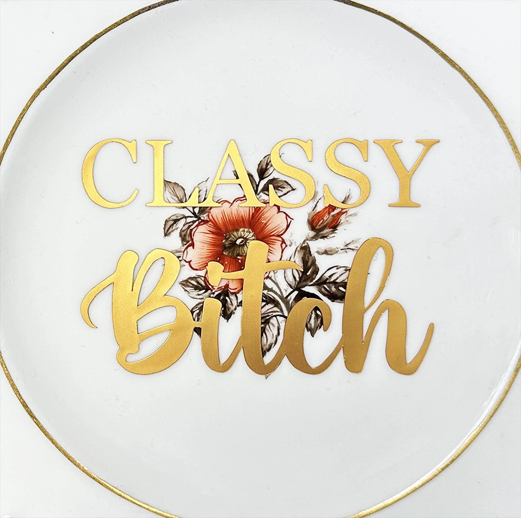 A vintage plate with a witty quote “classy bitch” in gold writing