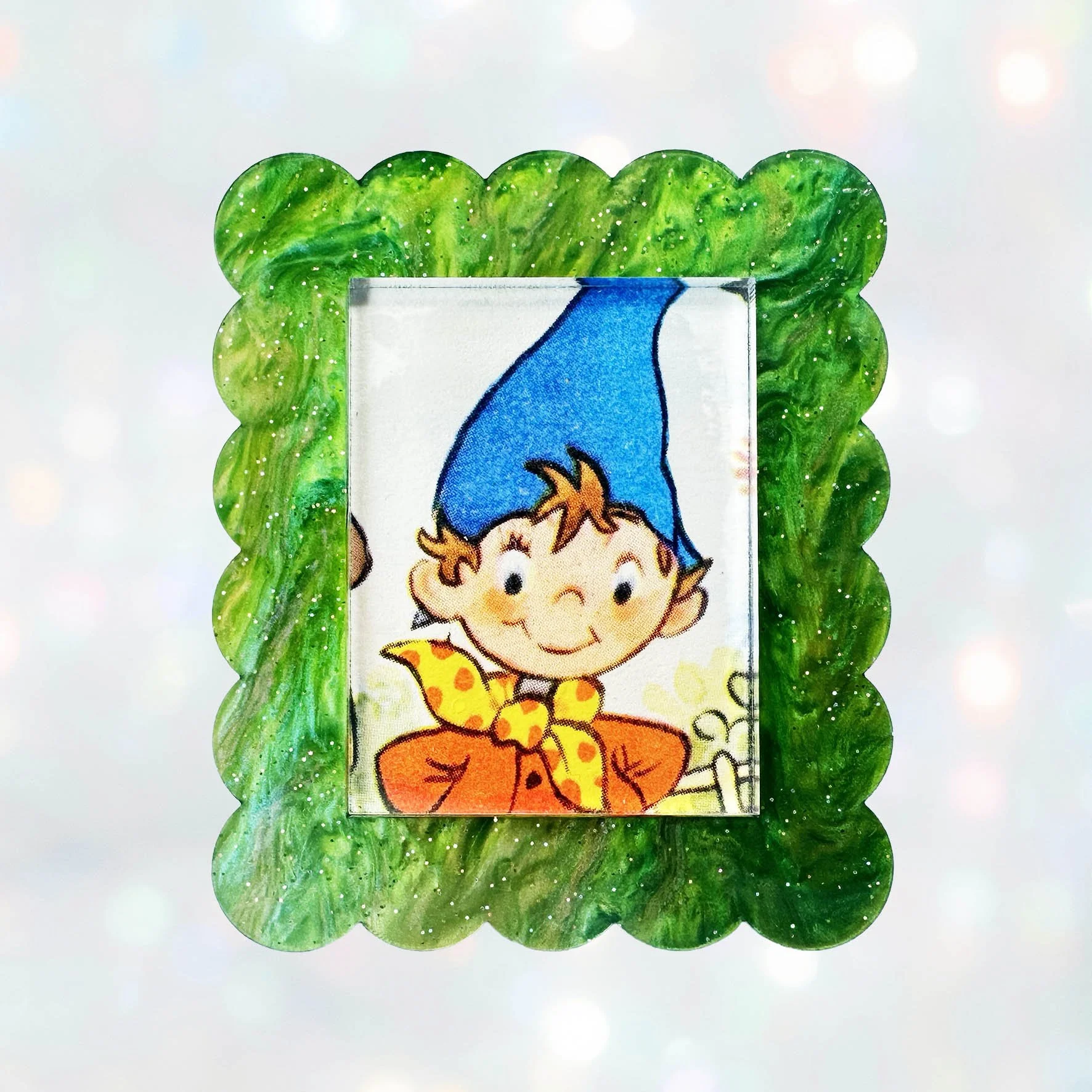 A green glitter acrylic brooch featuring a picture of Noddy