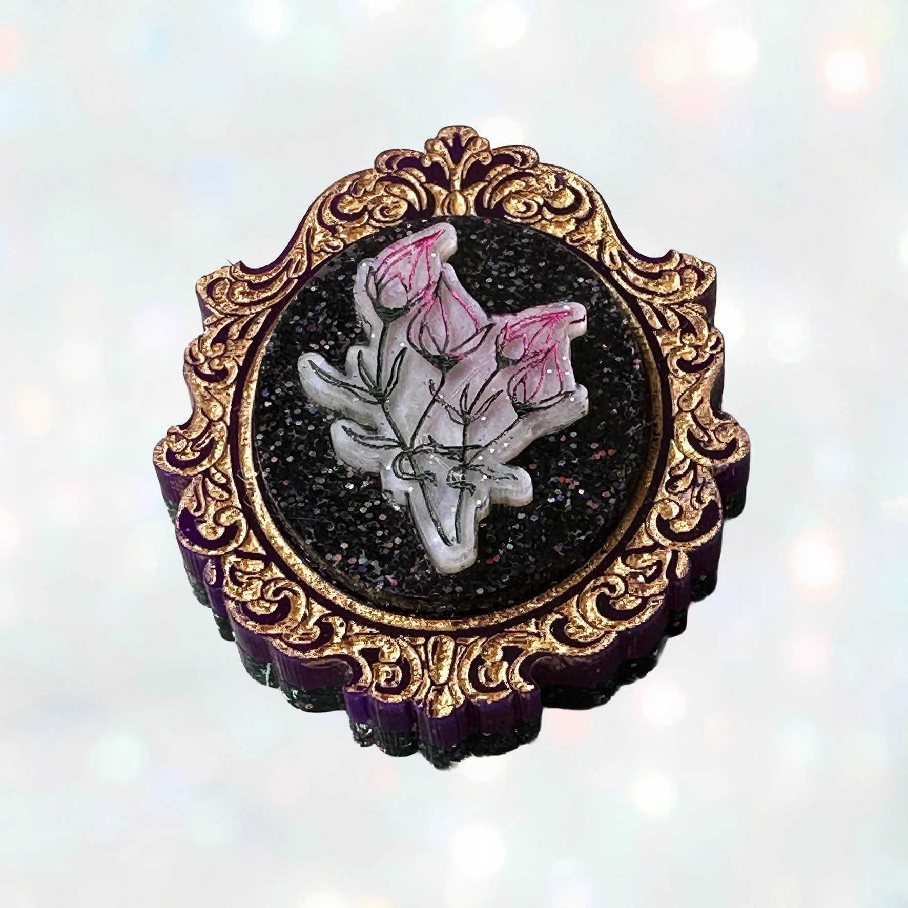 A laser cut acrylic cameo style brooch featuring a bunch of flowers within a purple and gold frame