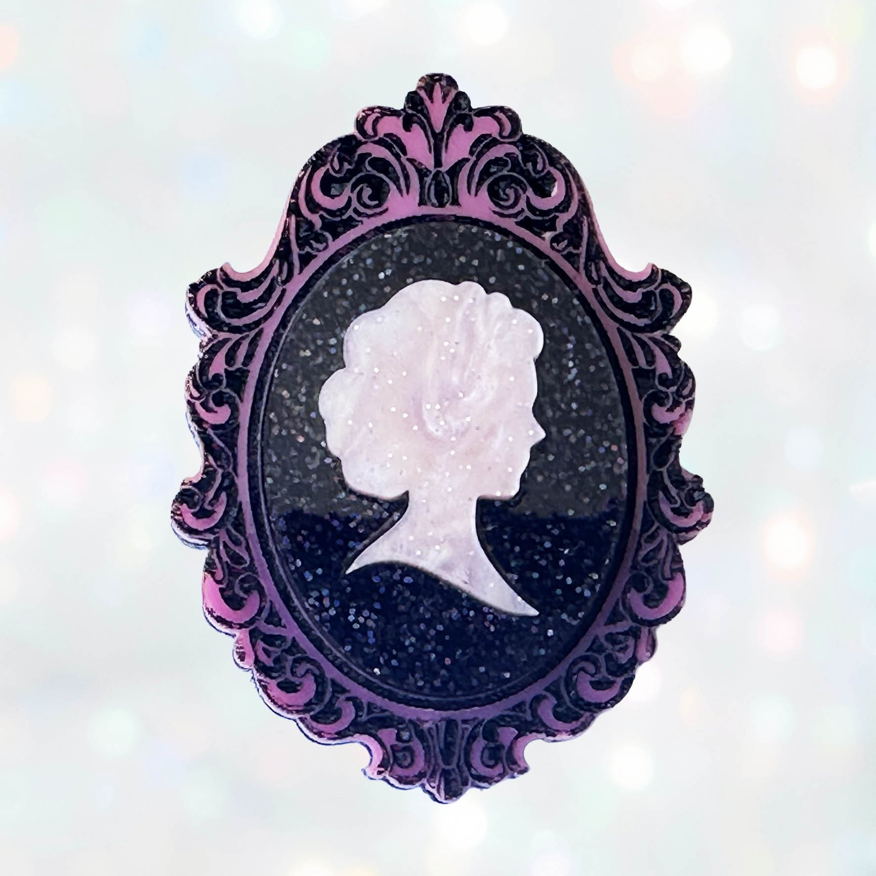 A pink and black glitter acrylic cameo style brooch featuring a silhouette