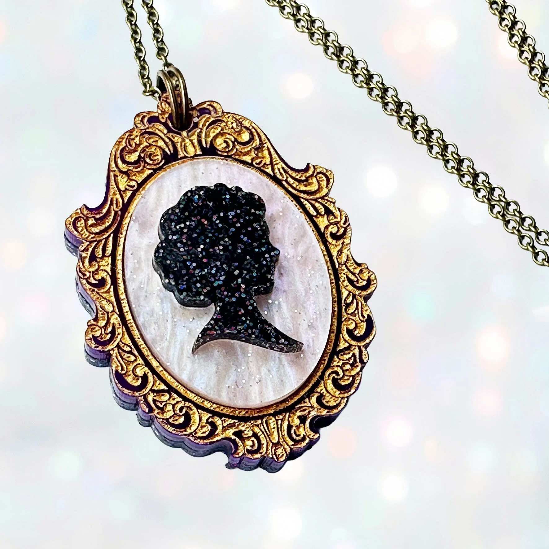A purple, pink and gold laser cut acrylic cameo style necklace featuring a silhouette