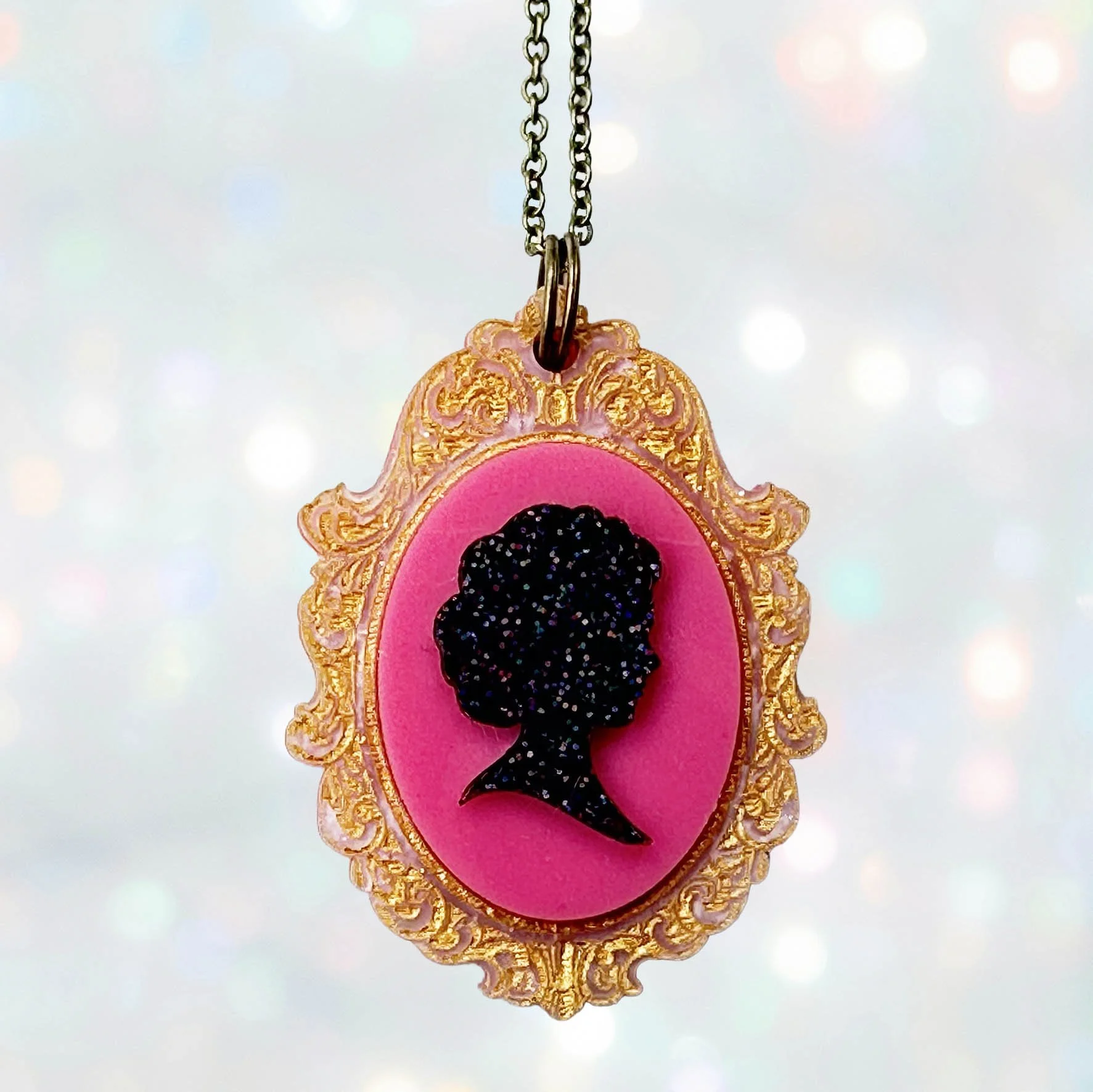 A pink, gold and black glitter laser cut acrylic cameo style necklace featuring a silhouette