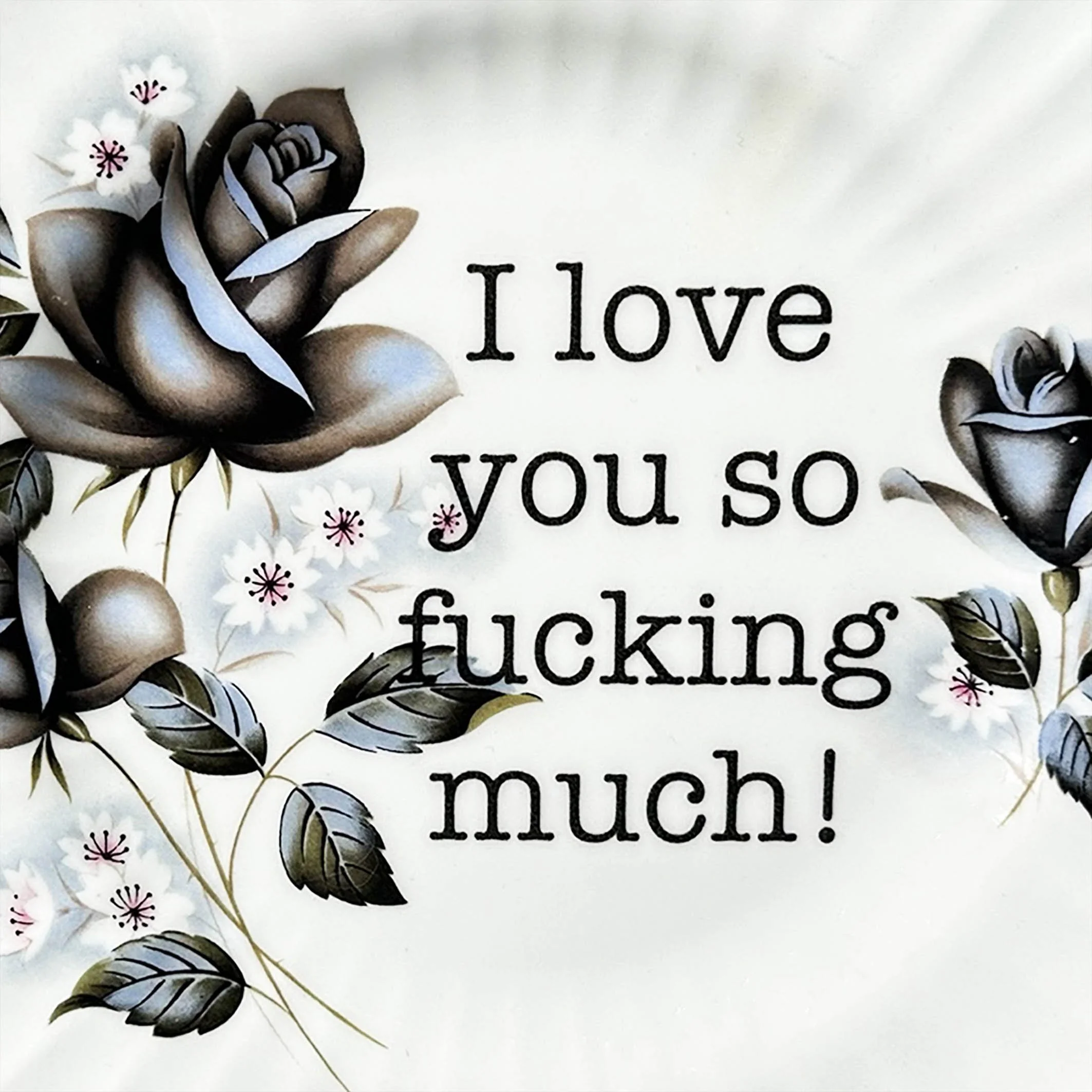 A vintage decorative wall plate with a black rose design and the words “I love you so fucking much!” in black typewriter style lettering