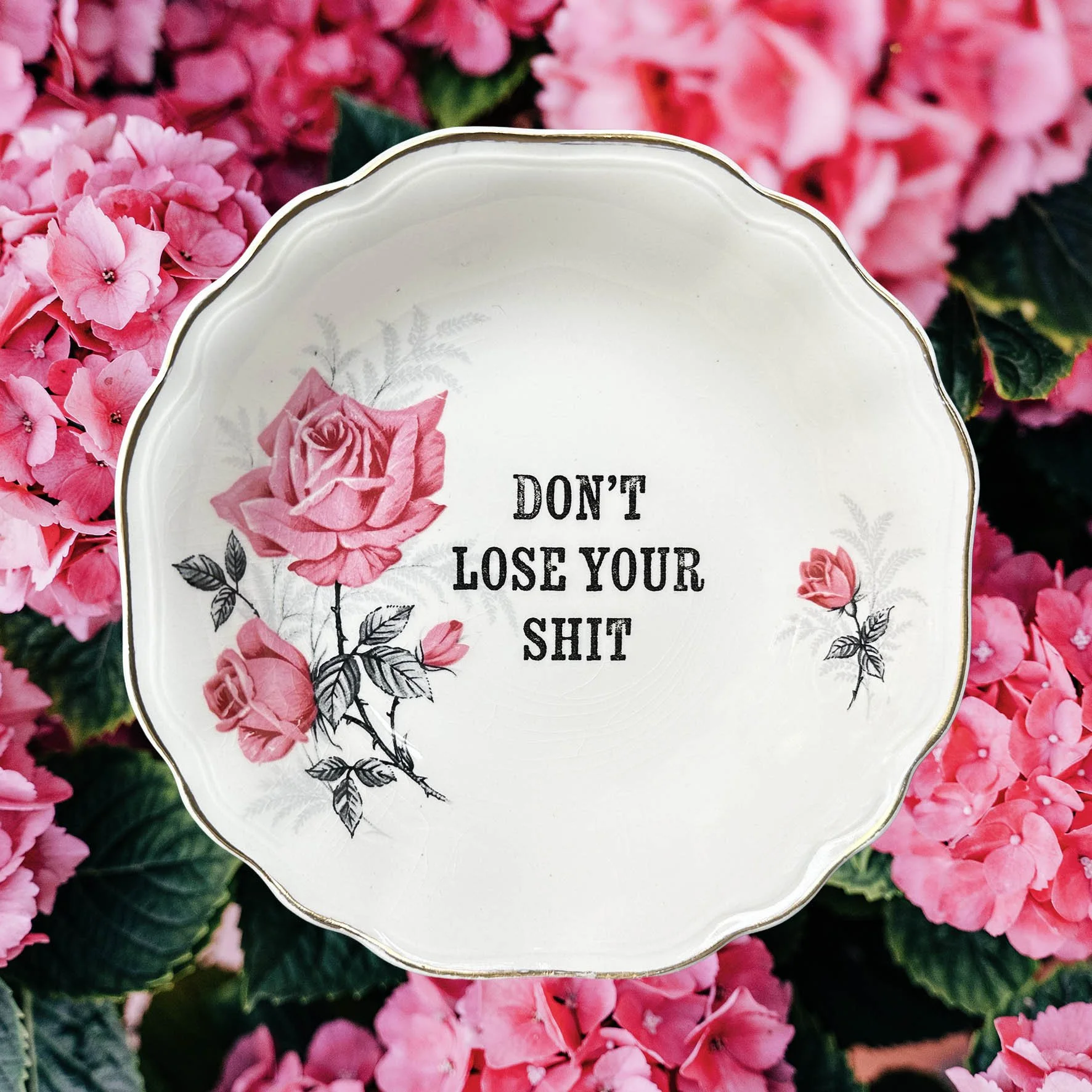 A vintage trinket dish with a pink floral design and the words “don’t lose your shit”
