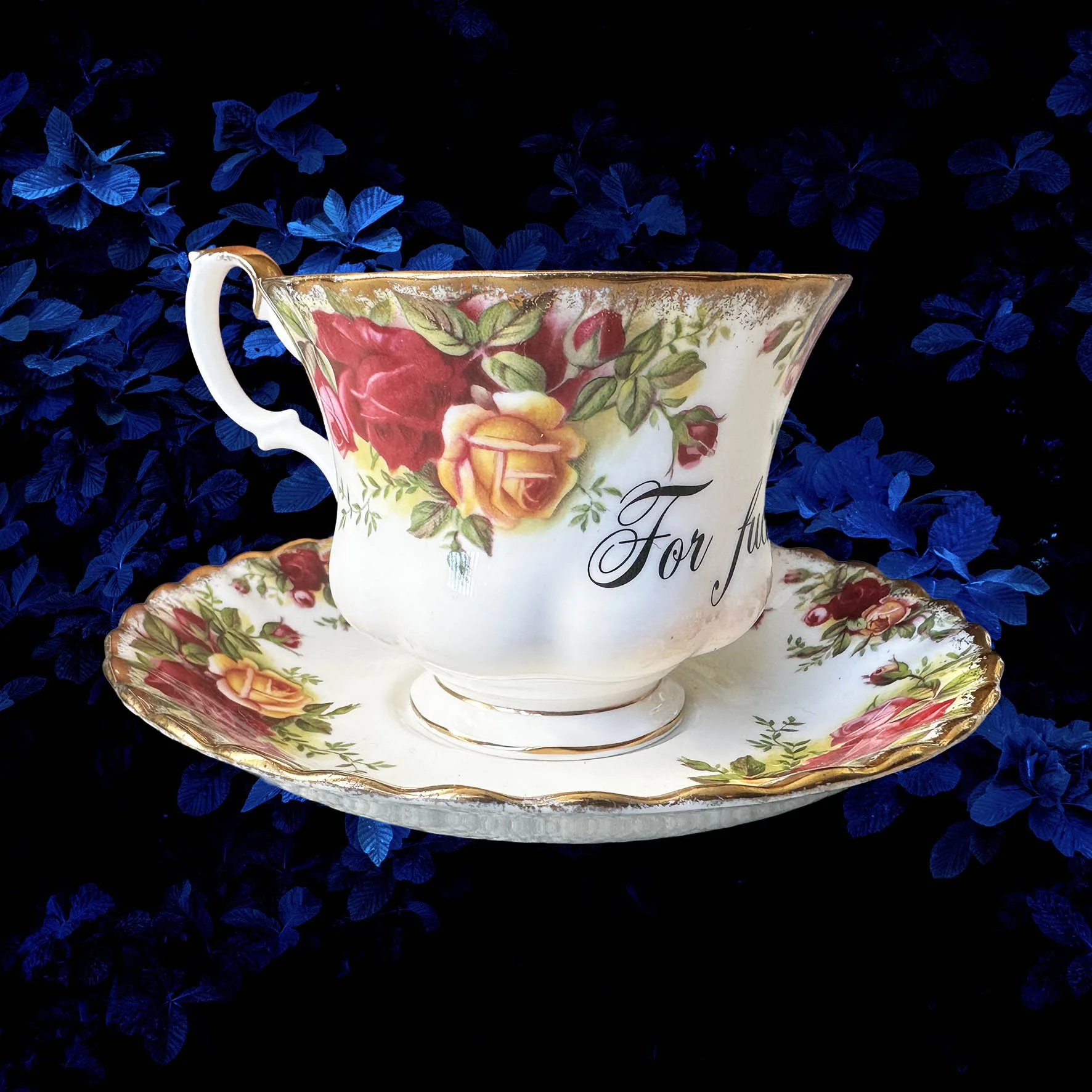 a vintage tea cup with a red rose design and the words "for fuck's sake" in black writing